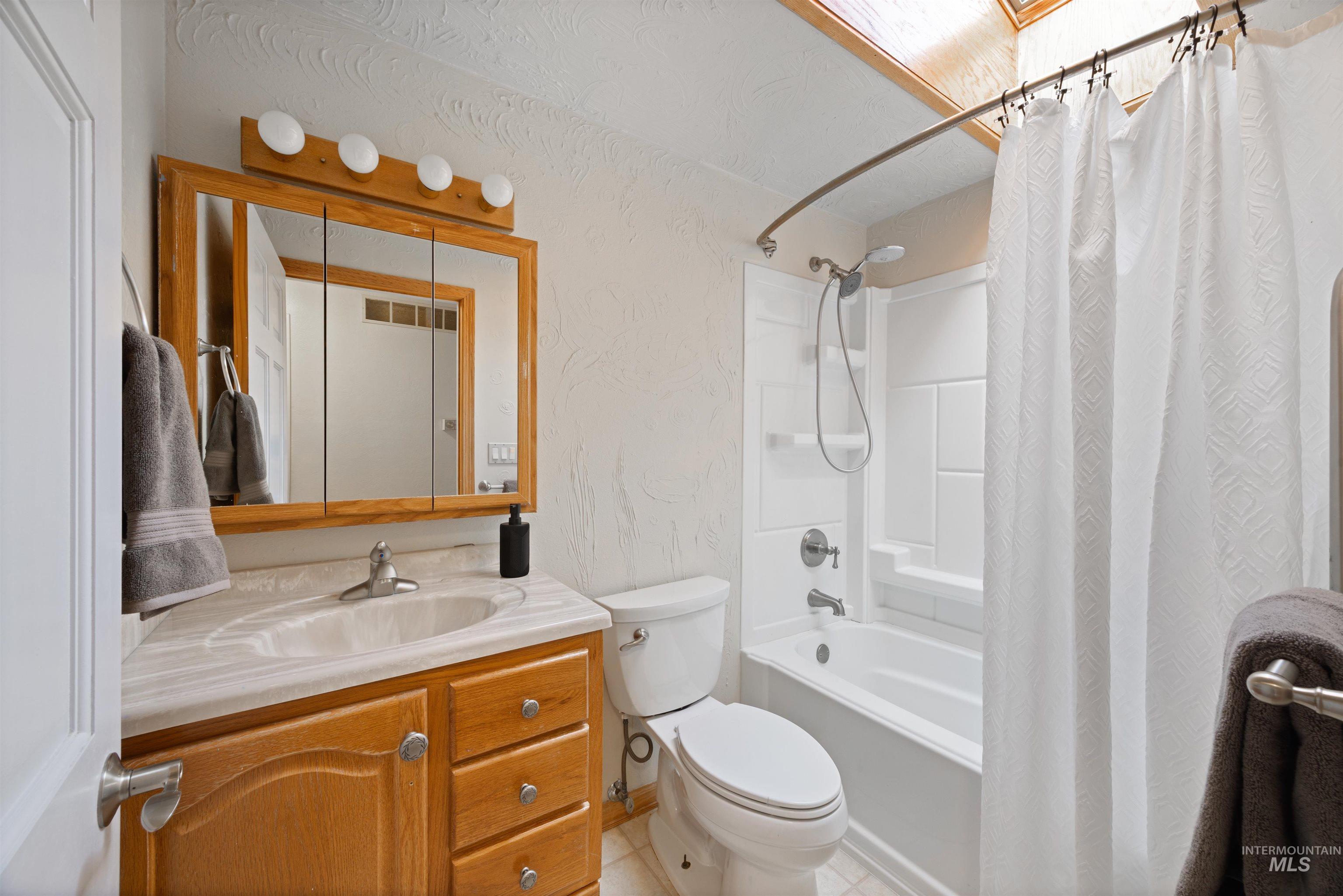 Full bath with shower / bathtub combination with curtain, a textured wall, vanity, and light tile patterned floors