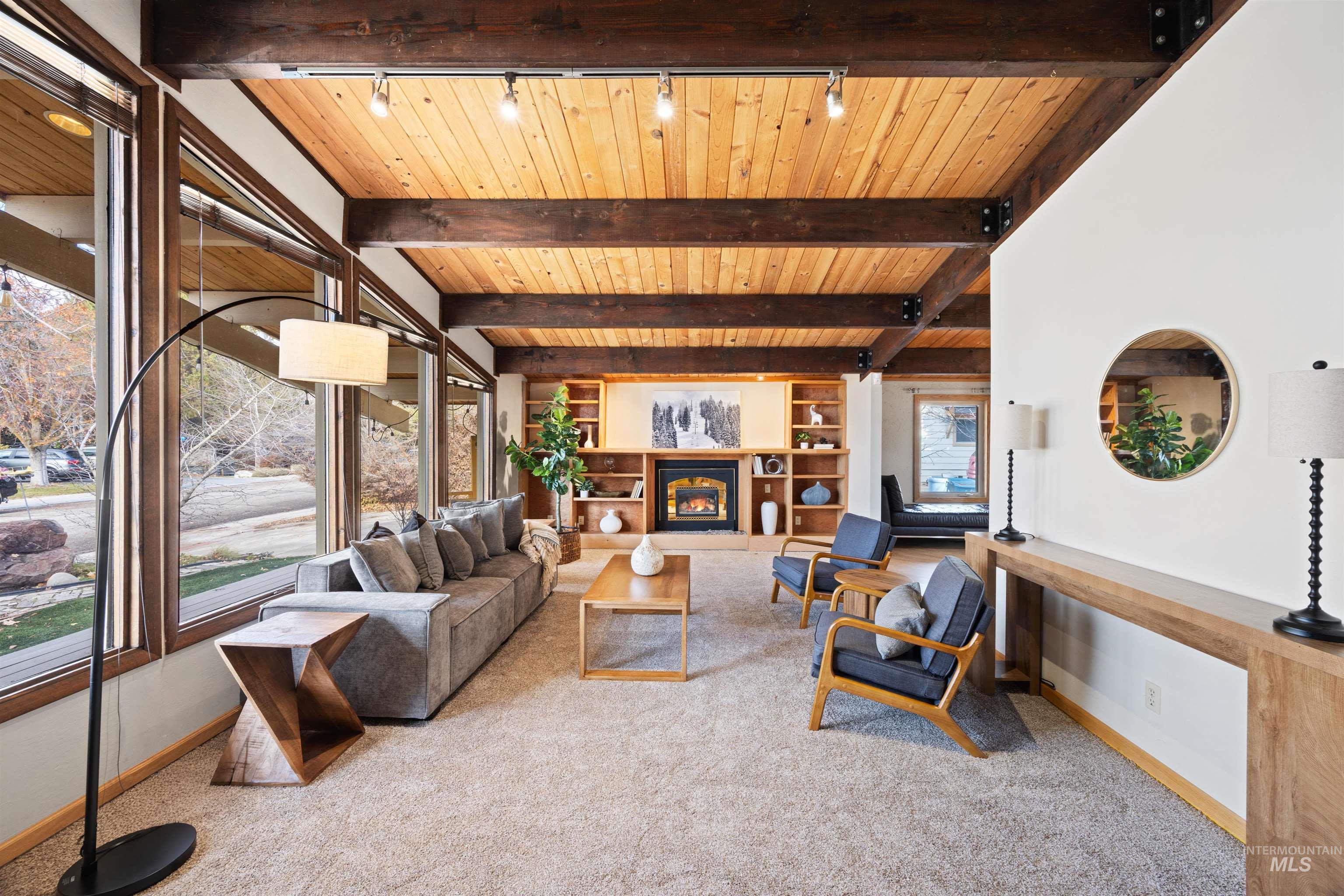 Carpeted living room with a warm lit fireplace, a wood ceiling with exposed beams, rail lighting, and built in features