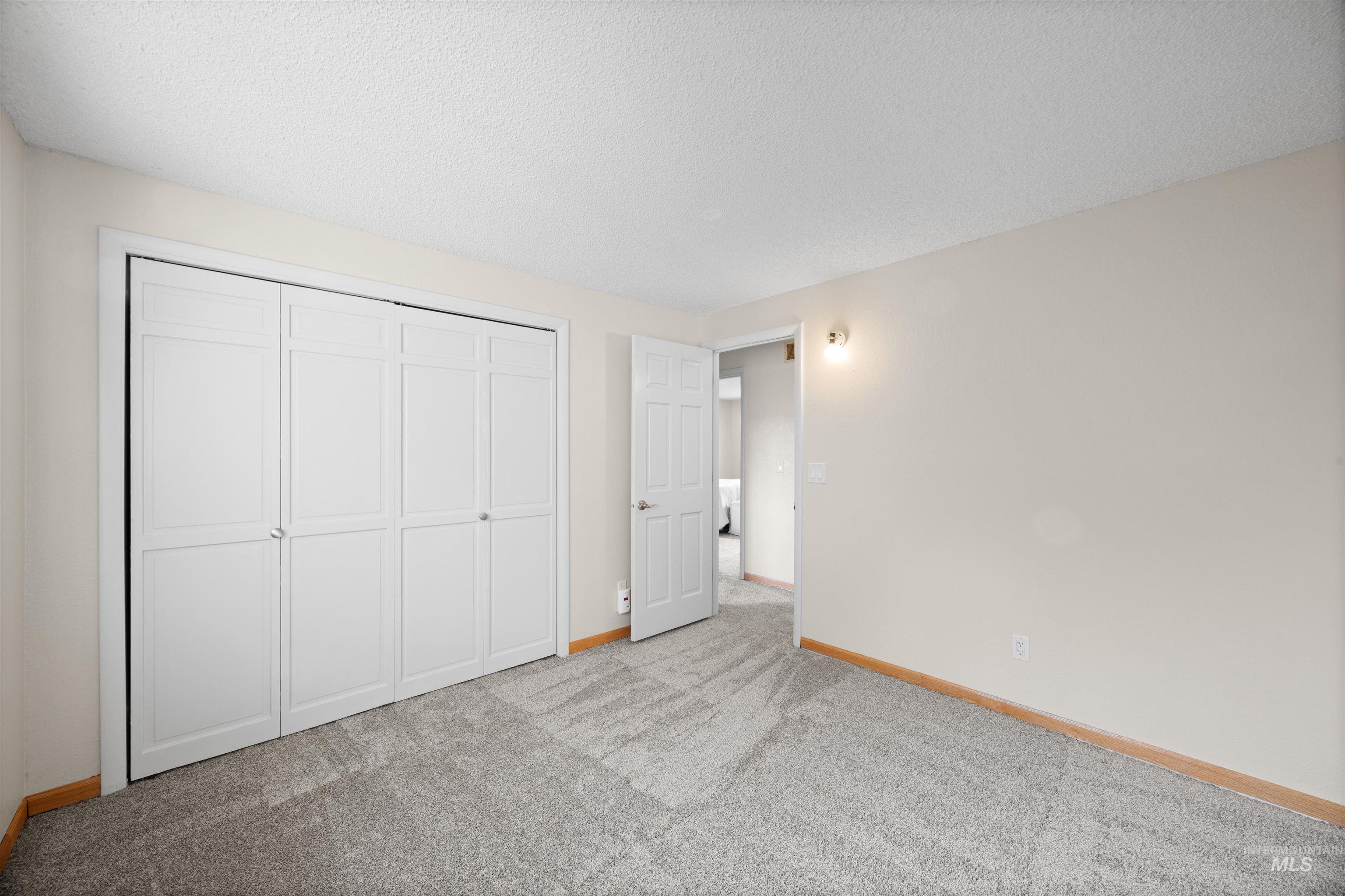 Unfurnished bedroom with a textured ceiling, light carpet, and a closet