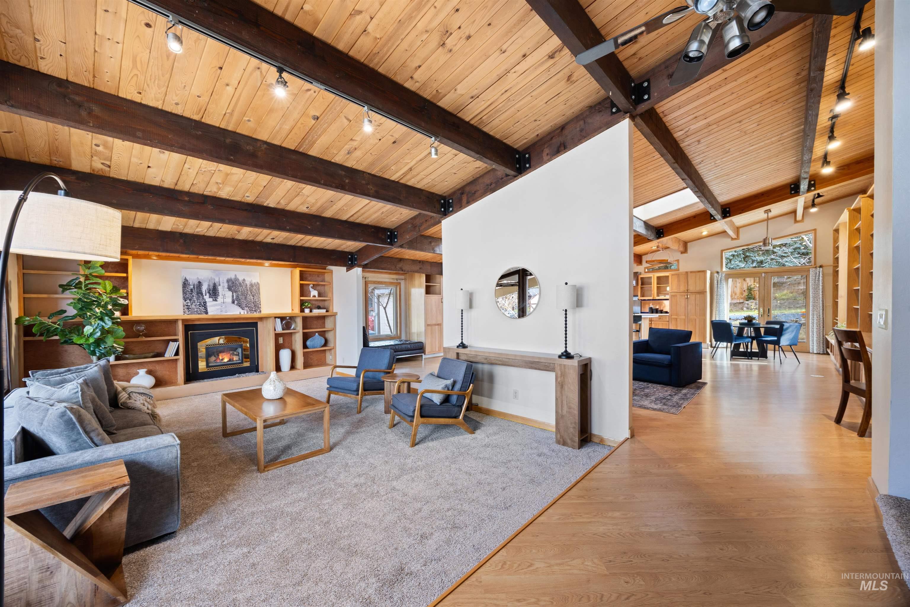 Living area featuring rail lighting, built in features, a glass covered fireplace, light wood-style floors, and wood ceiling