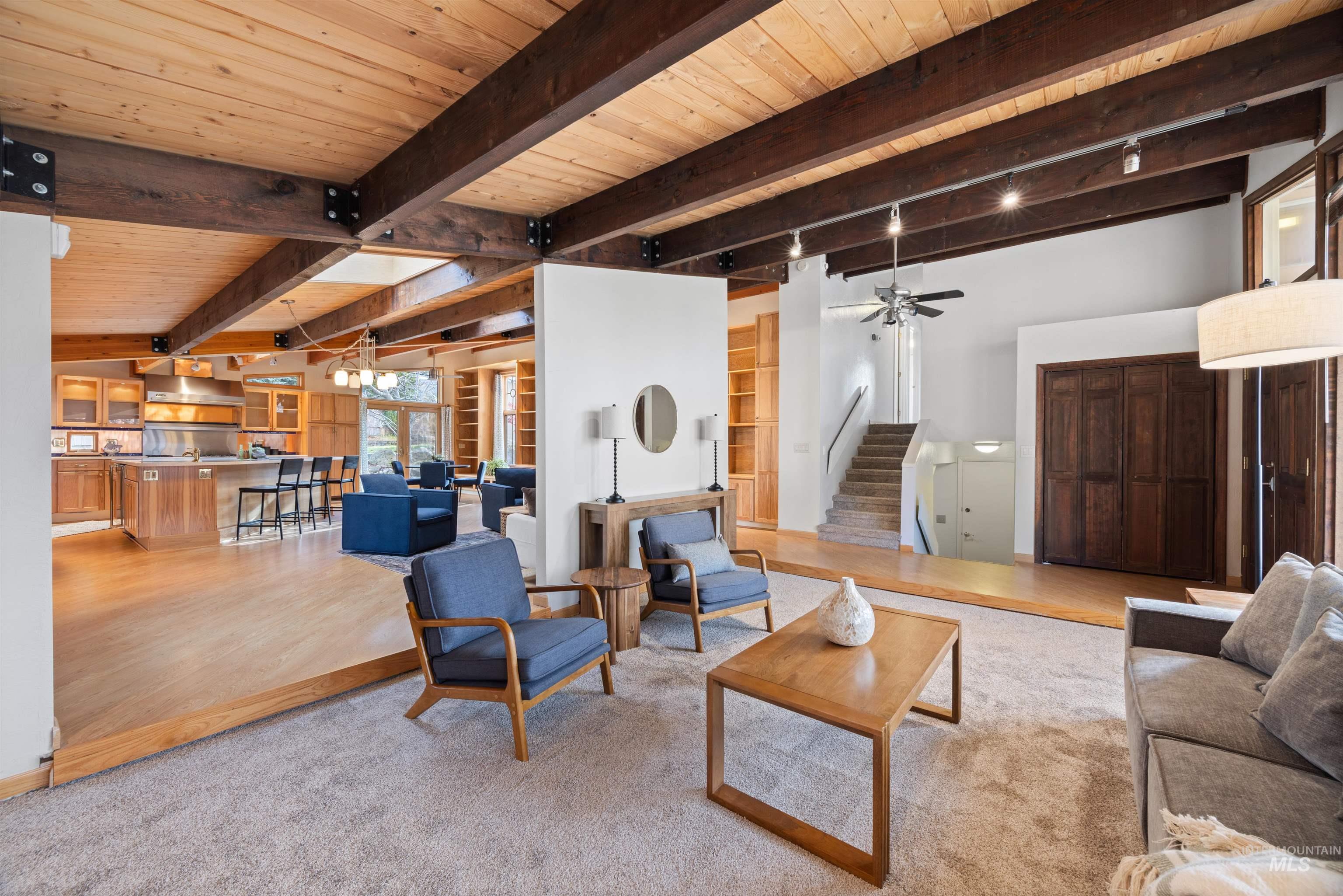 Living area with a wooden ceiling with exposed beams, a ceiling fan, stairs, light wood-style flooring, and a chandelier