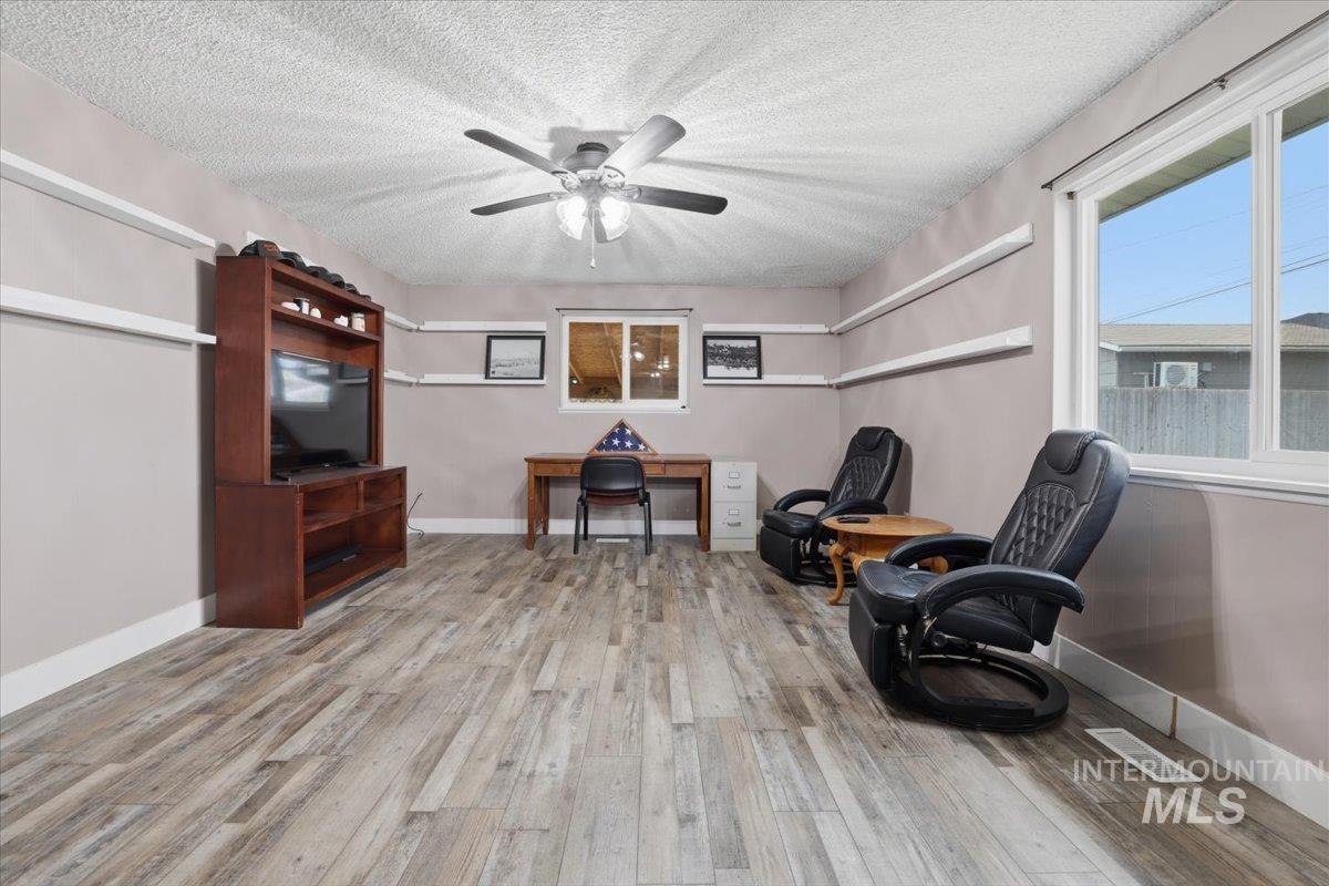 Living area with a textured ceiling, light wood finished floors, a ceiling fan, and an office area