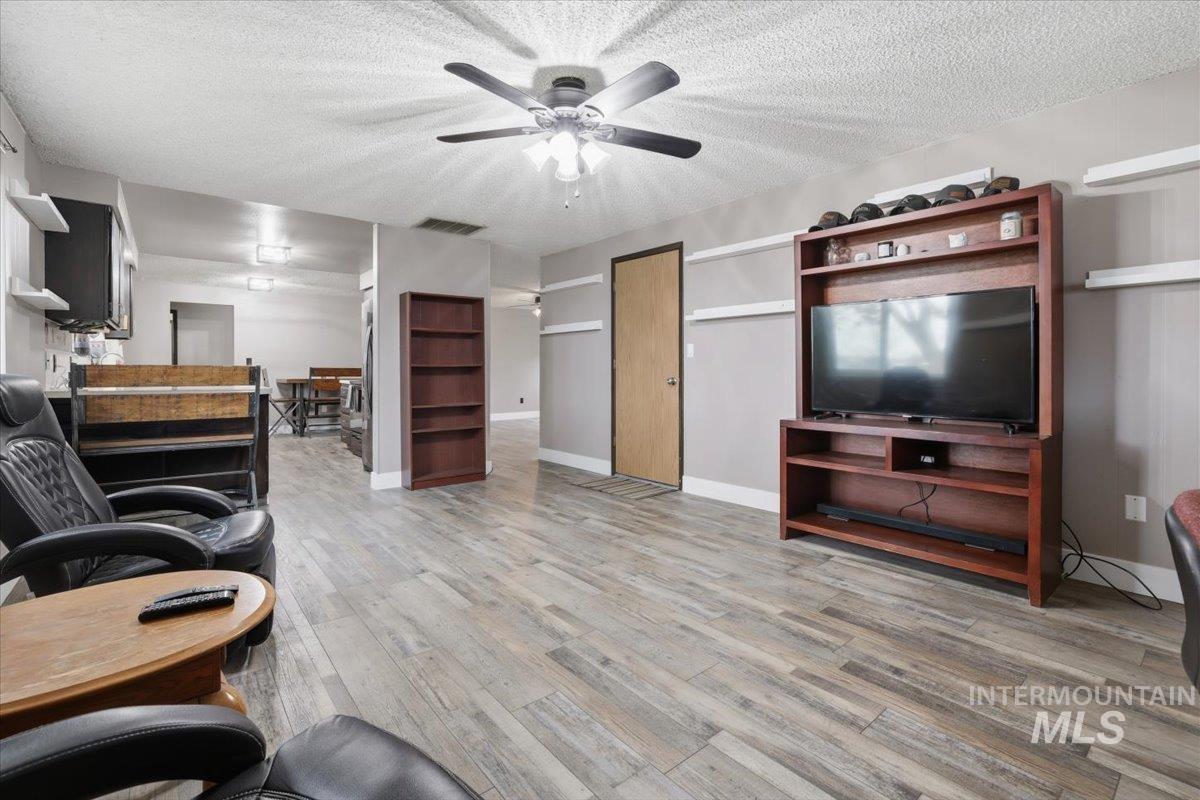 Living room with a textured ceiling, light wood-style floors, and a ceiling fan