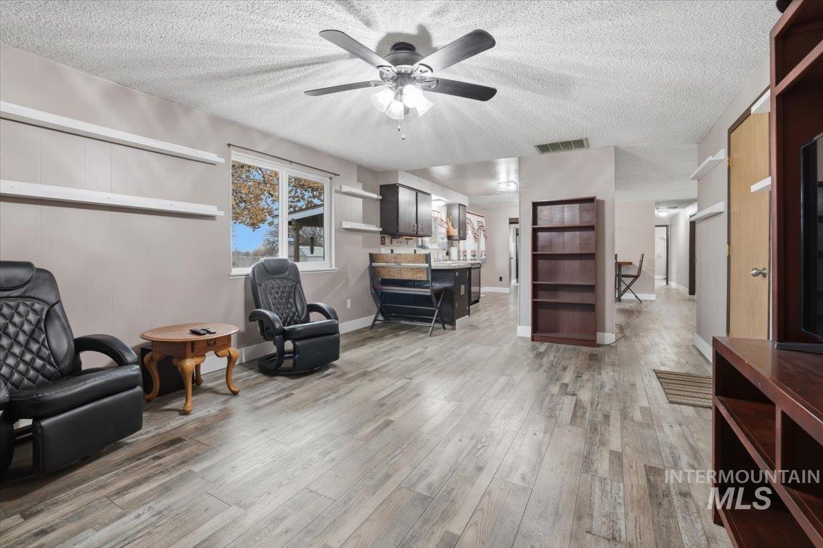 Living area with a textured ceiling, light wood-type flooring, and a ceiling fan