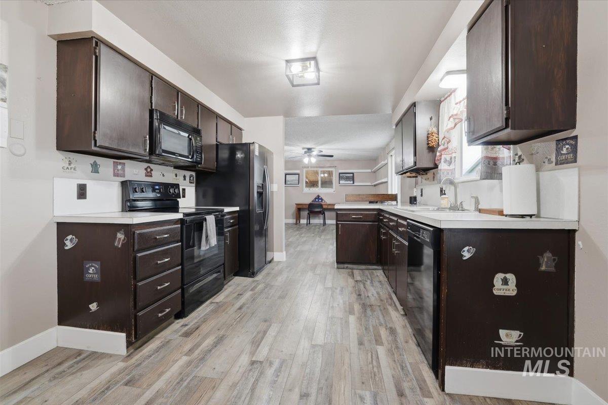 Kitchen with dark brown cabinets, black appliances, light countertops, light wood-style floors, and a peninsula
