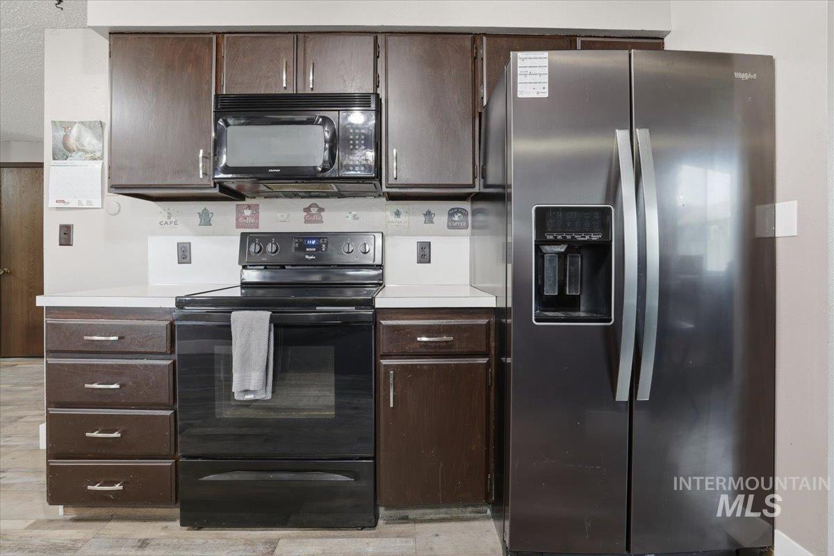 Kitchen with black appliances, dark brown cabinets, light countertops, and light wood finished floors