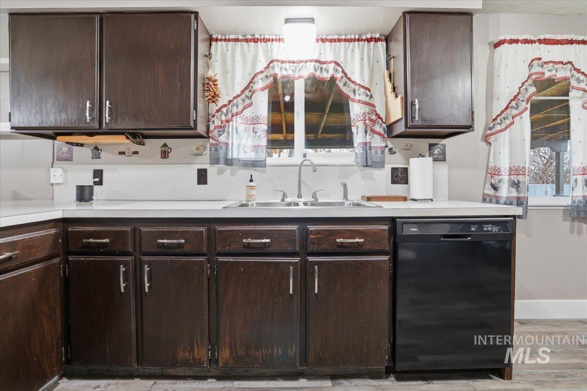 Kitchen with dark brown cabinets, black dishwasher, light countertops, and light wood-type flooring