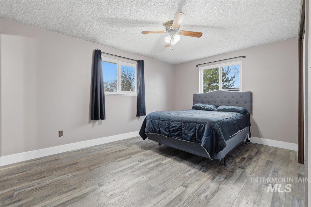 Bedroom with a textured ceiling, wood finished floors, ceiling fan, and multiple windows