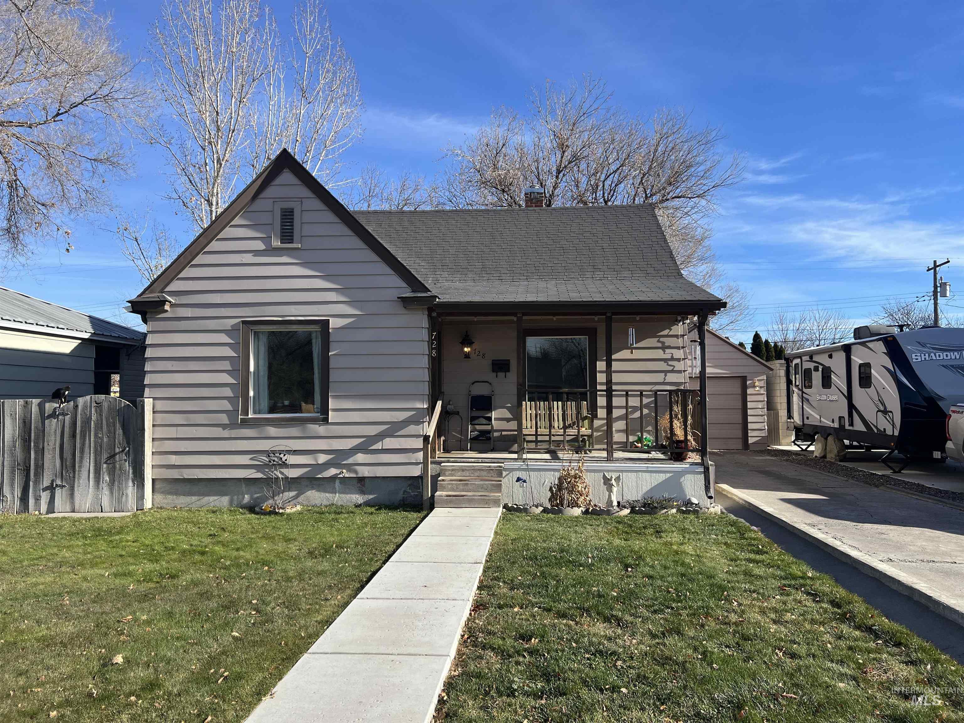 Bungalow-style home with covered porch, a front yard, a chimney, an outdoor structure, and driveway