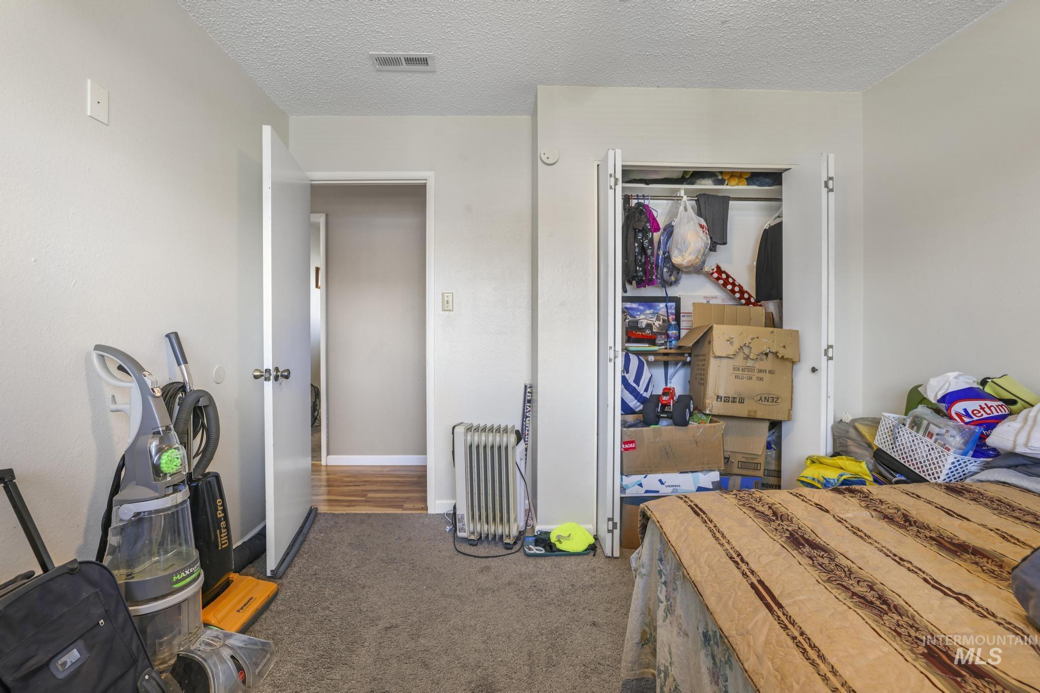 Carpeted bedroom featuring radiator heating unit, a textured ceiling, and a closet