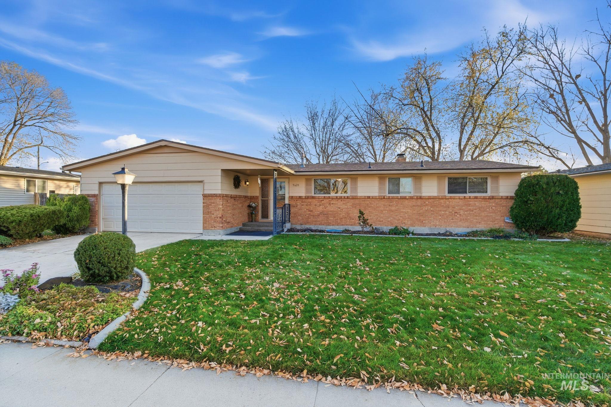 Ranch-style home featuring brick siding, a front yard, driveway, a garage, and a chimney