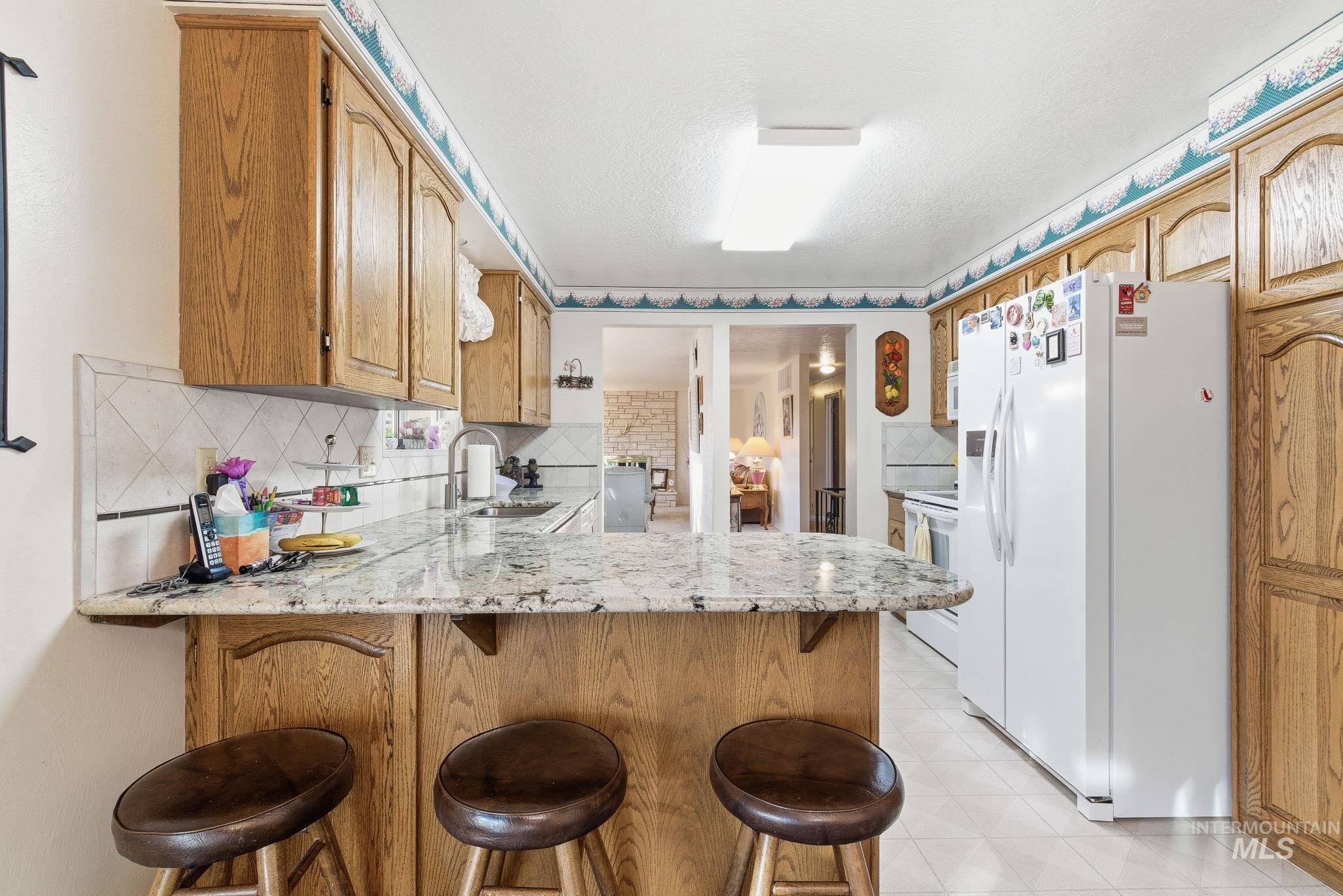 Kitchen with a peninsula, white appliances, light stone countertops, a kitchen bar, and decorative backsplash