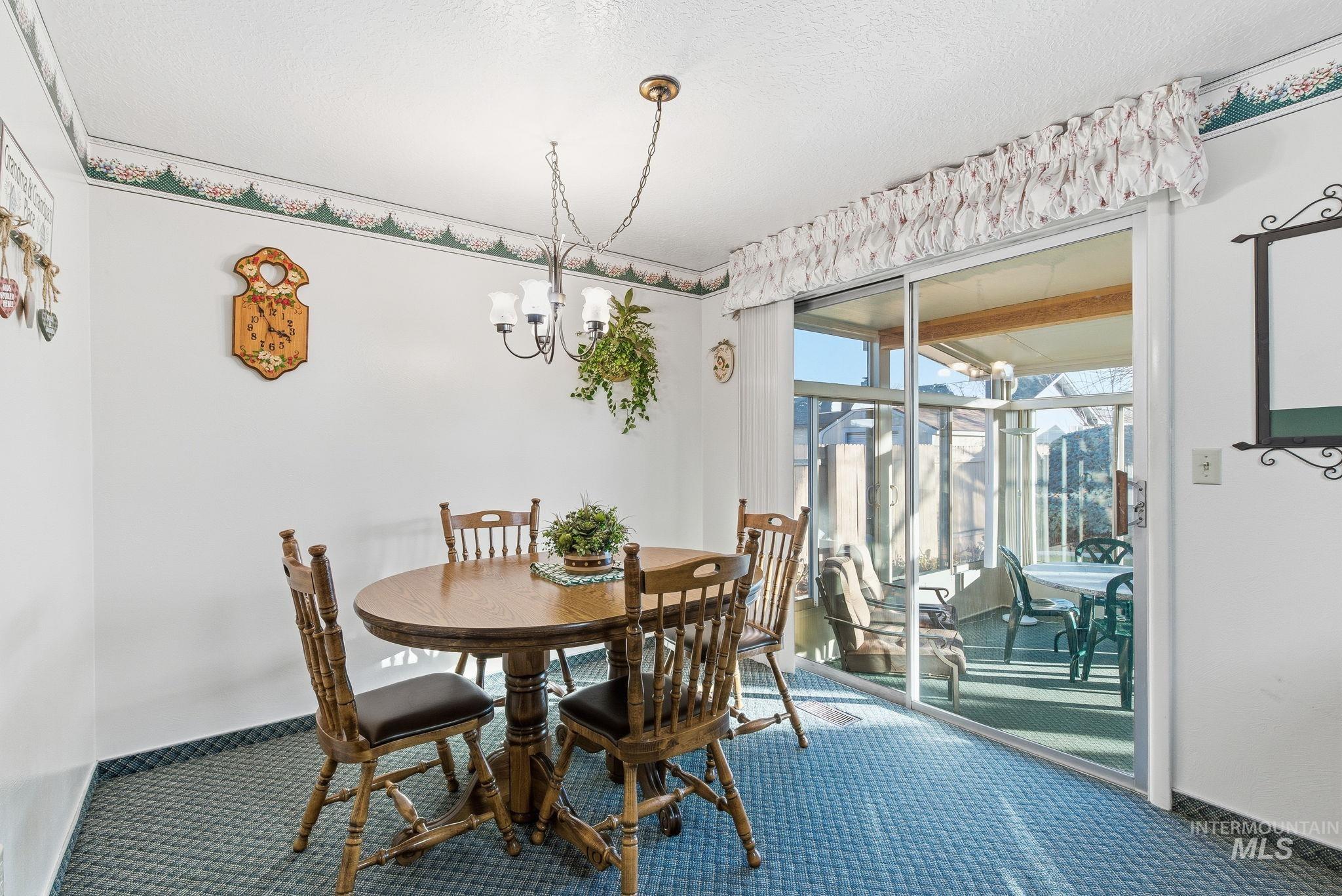 Carpeted dining area featuring a chandelier and a textured ceiling