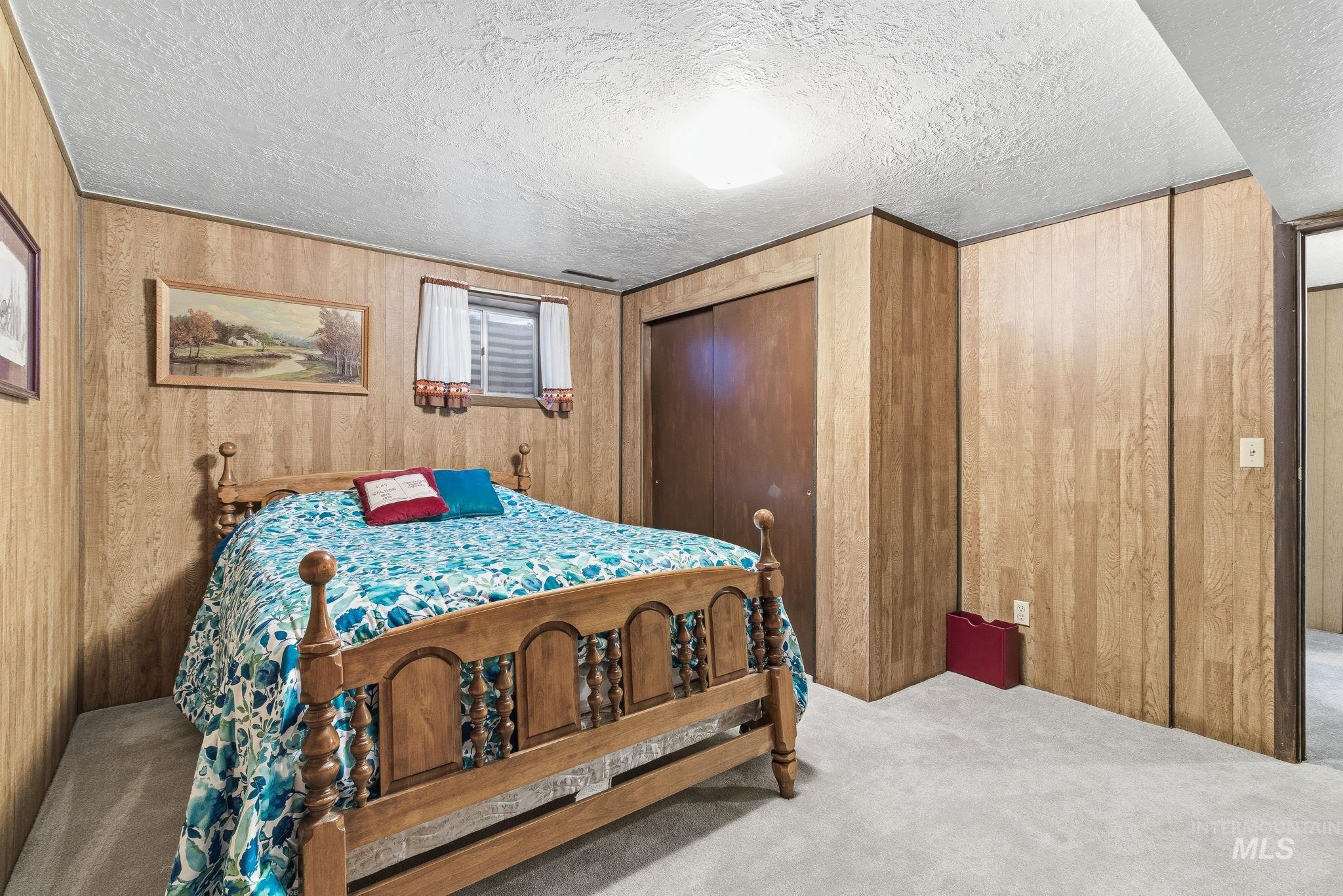 Carpeted bedroom featuring wooden walls, a textured ceiling, and a closet