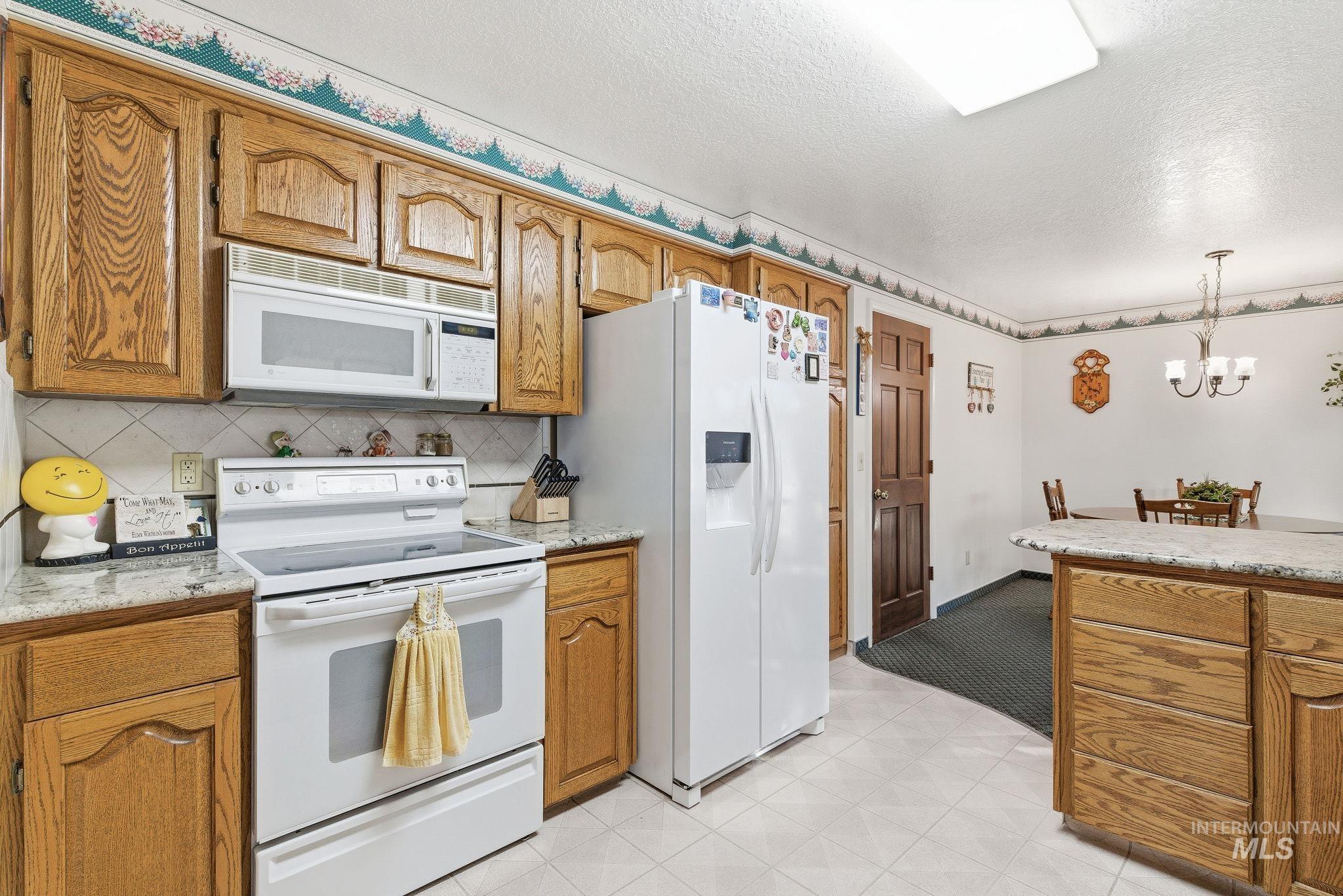 Kitchen with white appliances, brown cabinetry, a textured ceiling, decorative light fixtures, and decorative backsplash
