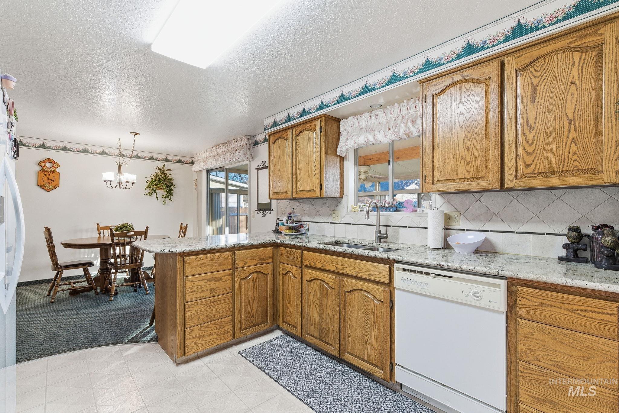 Kitchen featuring brown cabinetry, a peninsula, white appliances, light stone counters, and a textured ceiling