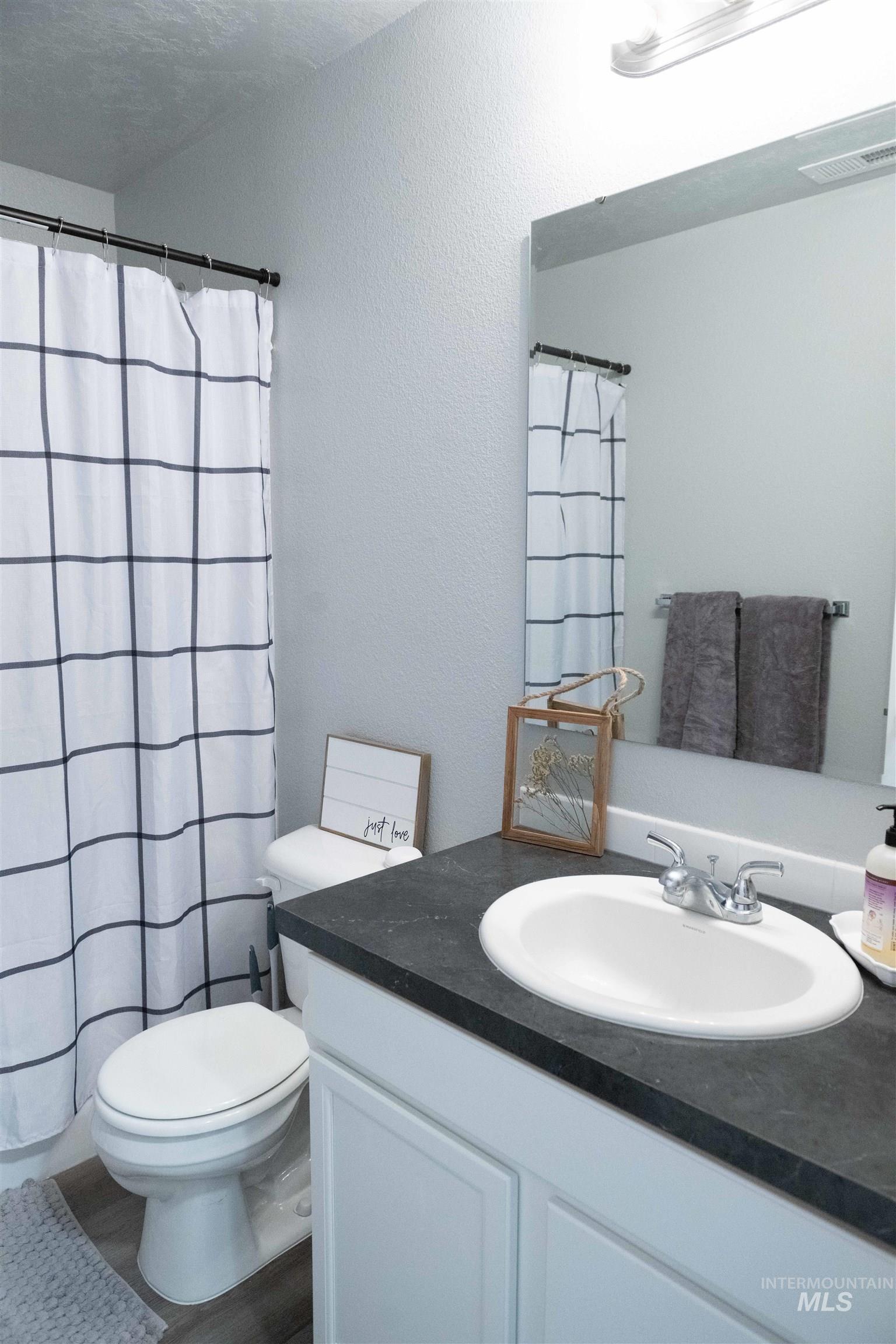 Bathroom featuring vanity, wood finished floors, a textured wall, and a shower with curtain
