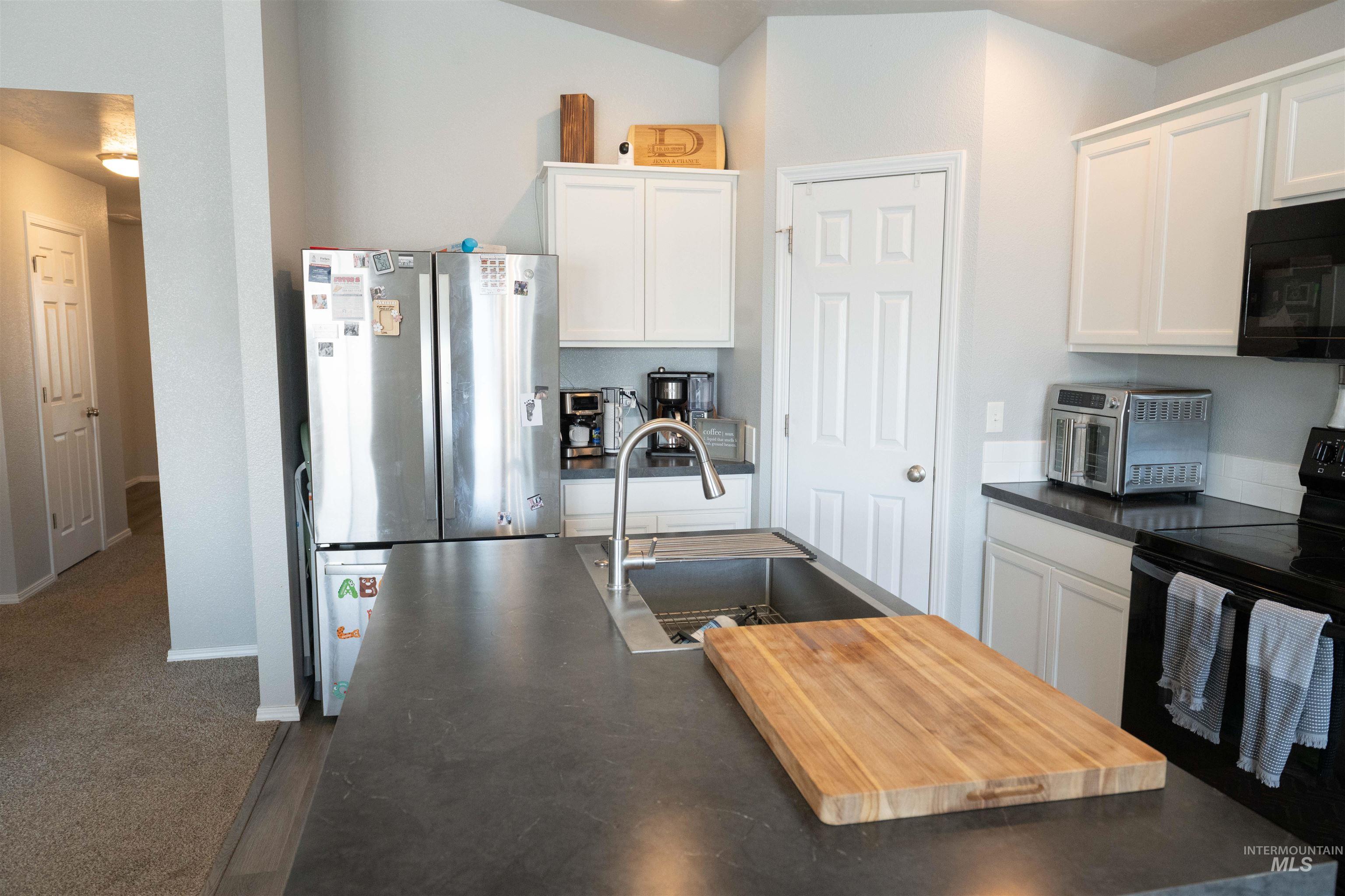 Kitchen featuring black appliances, dark countertops, and white cabinetry