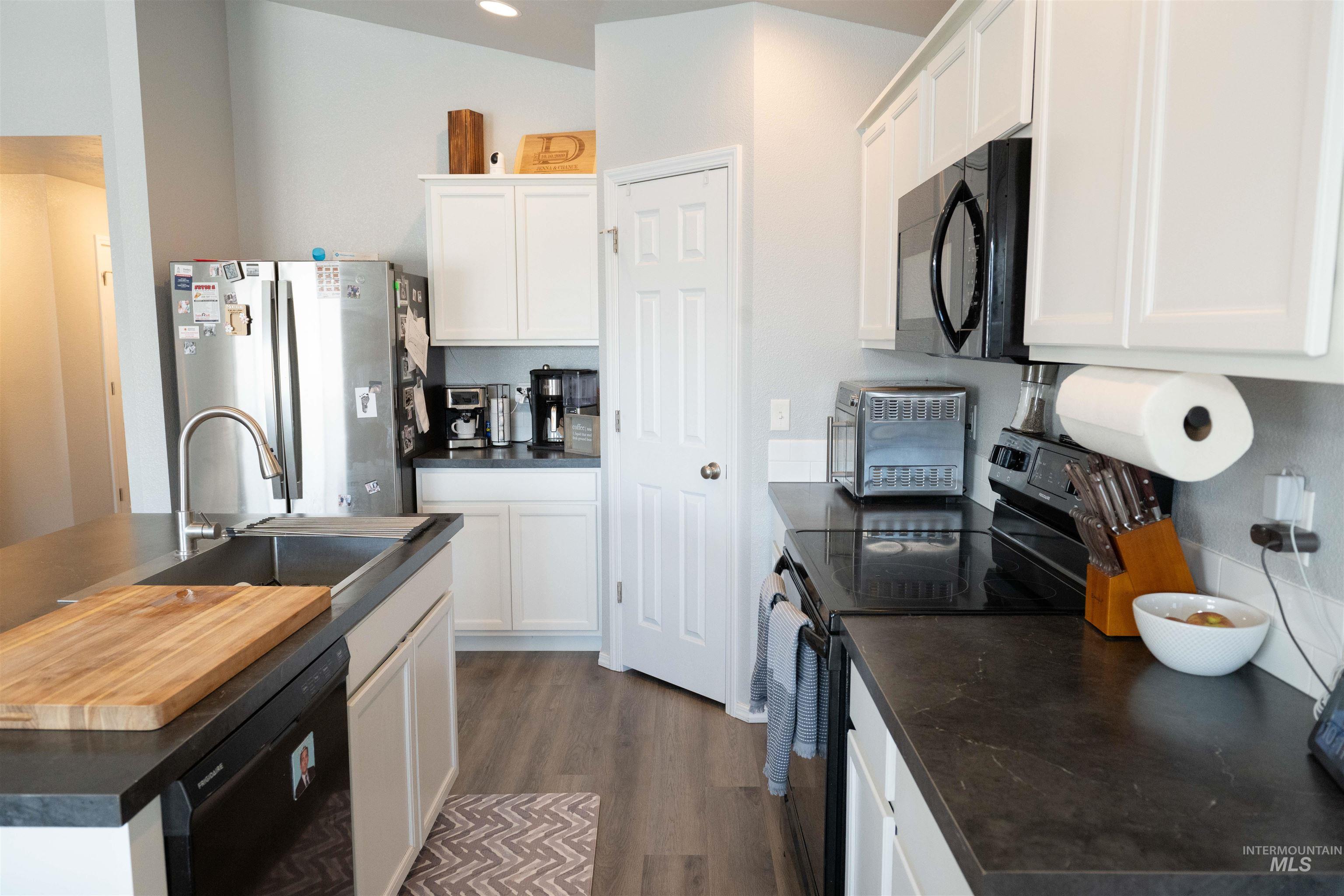 Kitchen featuring black appliances, dark countertops, dark wood finished floors, an island with sink, and white cabinets