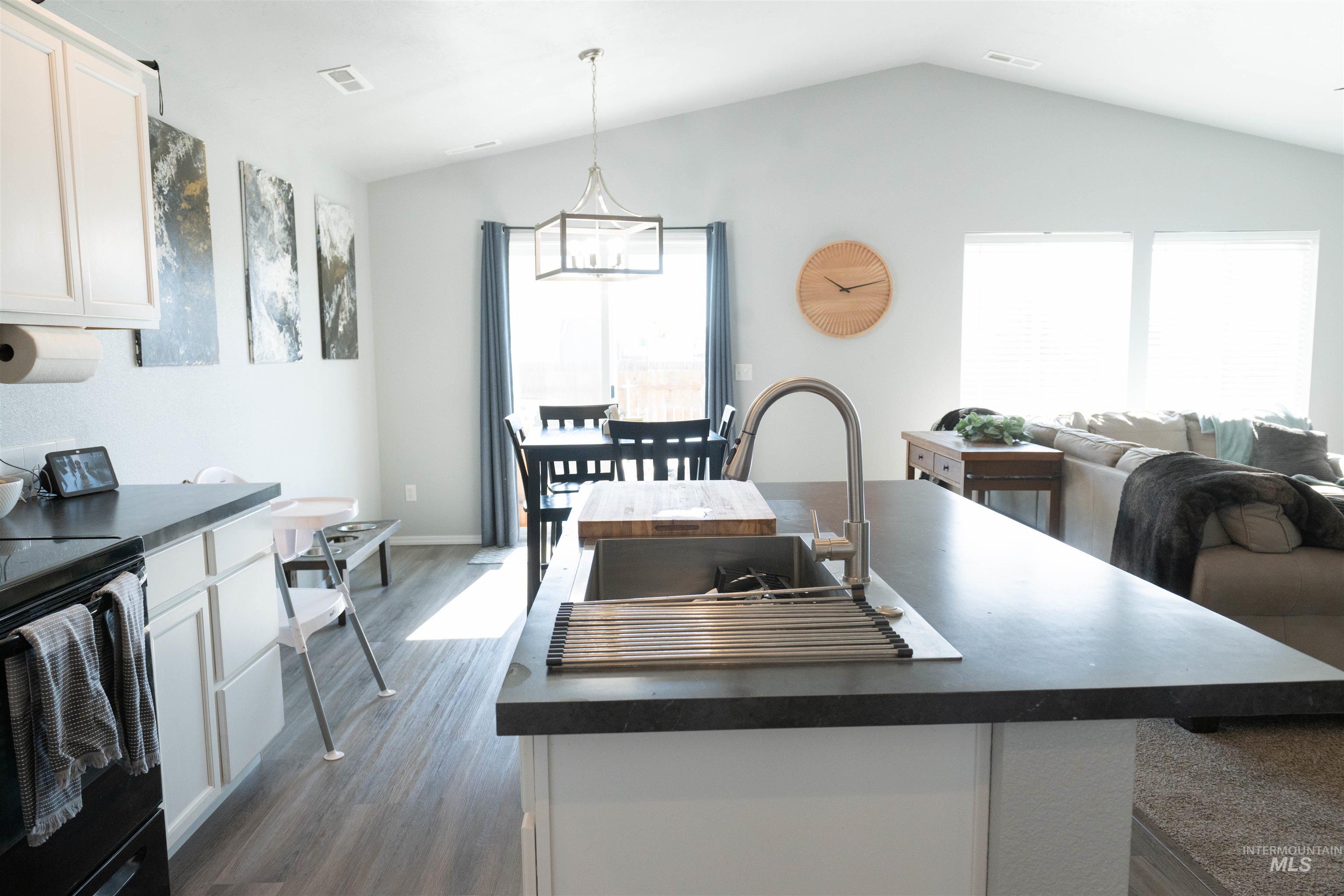 Kitchen featuring dark countertops, electric range, healthy amount of natural light, white cabinetry, and lofted ceiling
