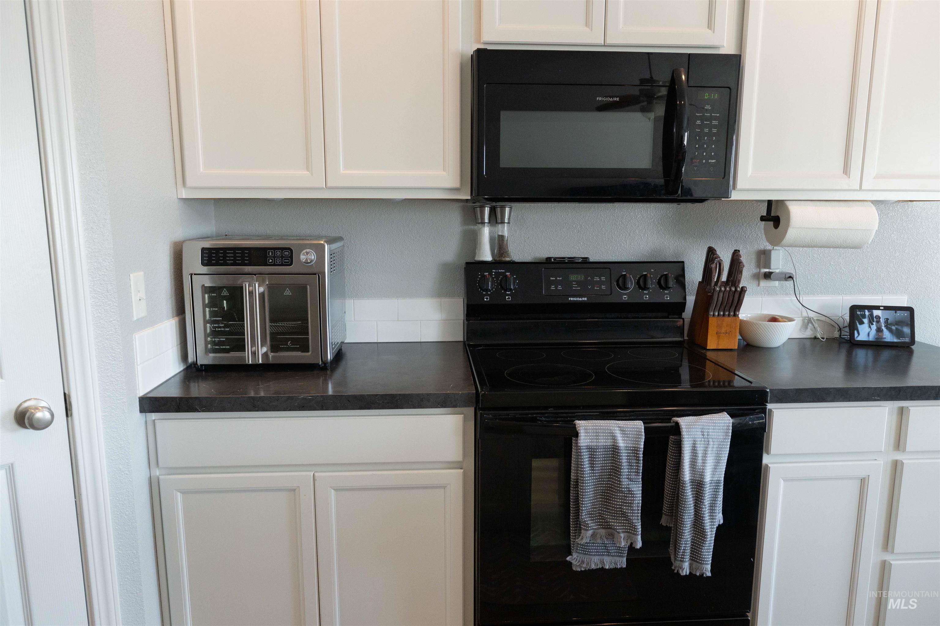 Kitchen with black appliances, white cabinetry, and dark countertops