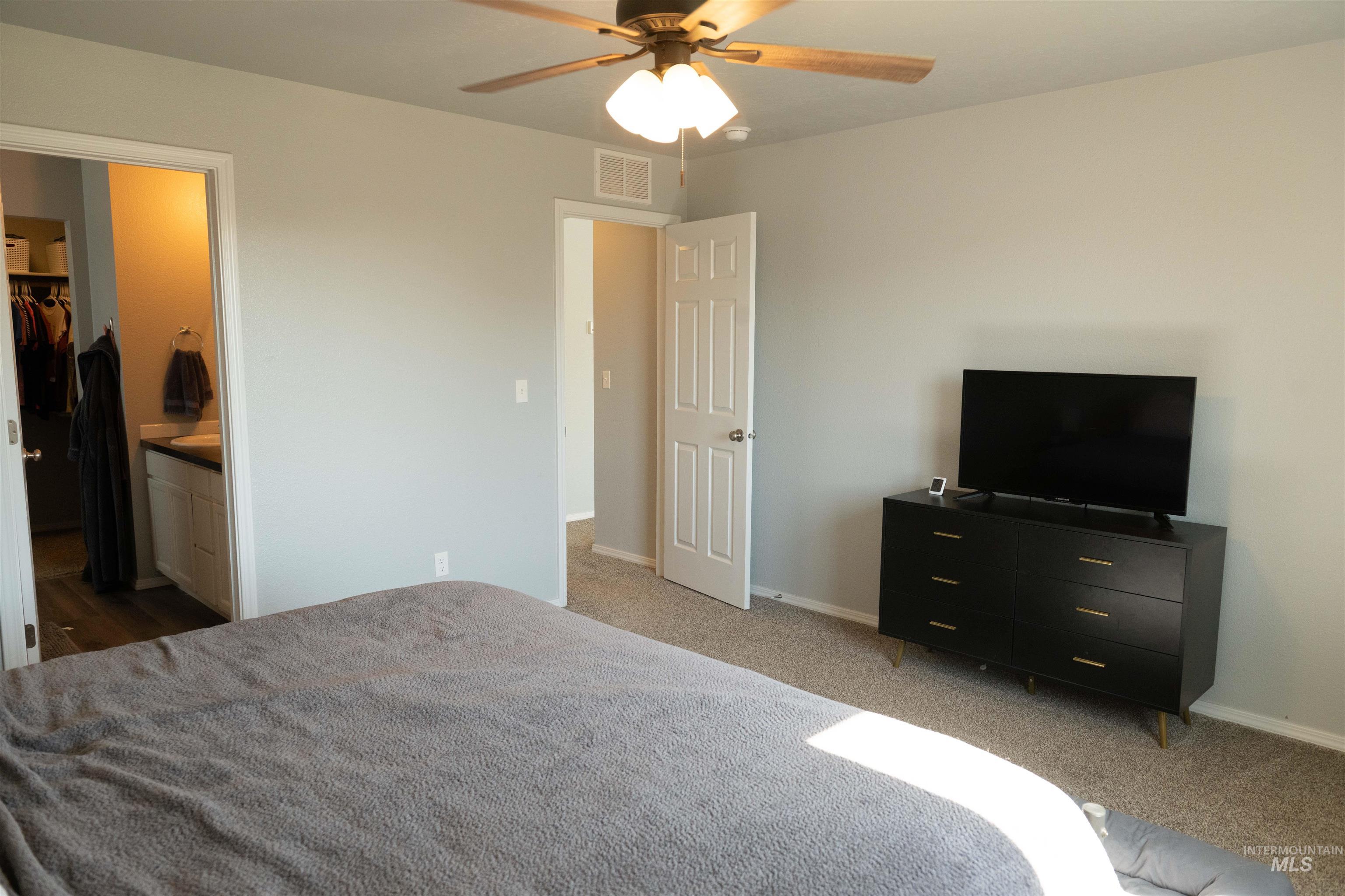 Carpeted bedroom with ceiling fan and connected bathroom