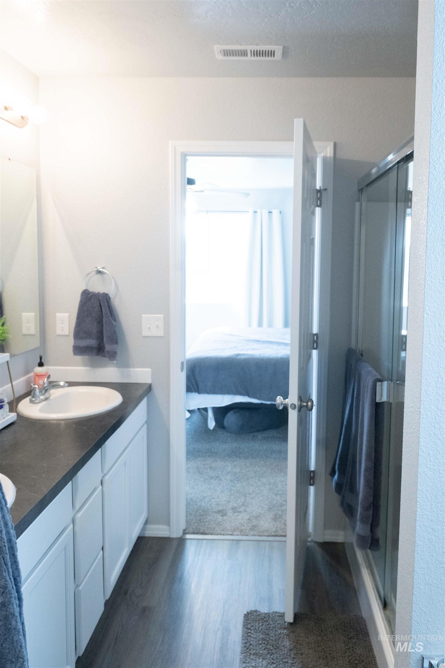 Ensuite bathroom featuring double vanity, a stall shower, and wood finished floors