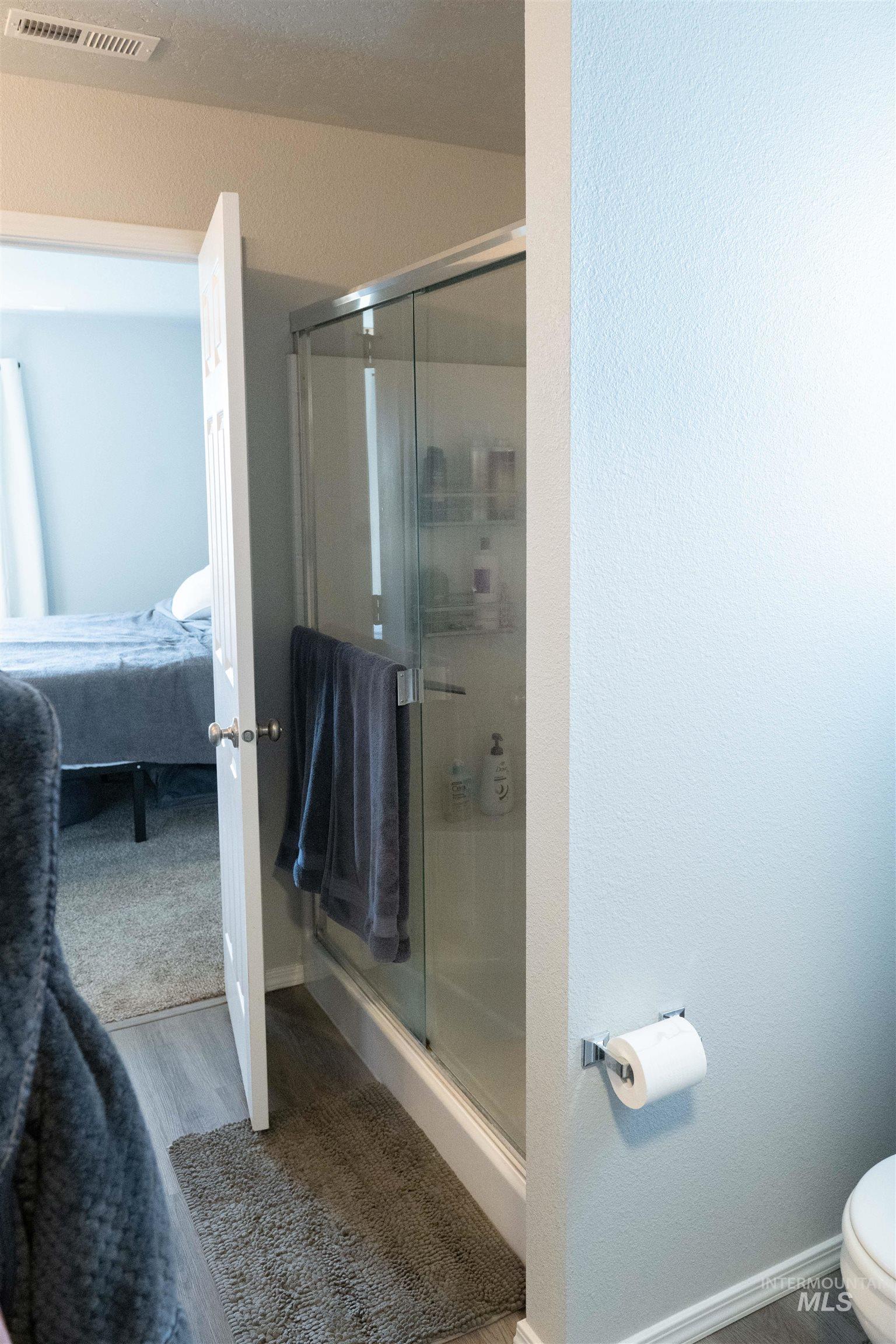 Ensuite bathroom with a stall shower, wood finished floors, and a textured wall