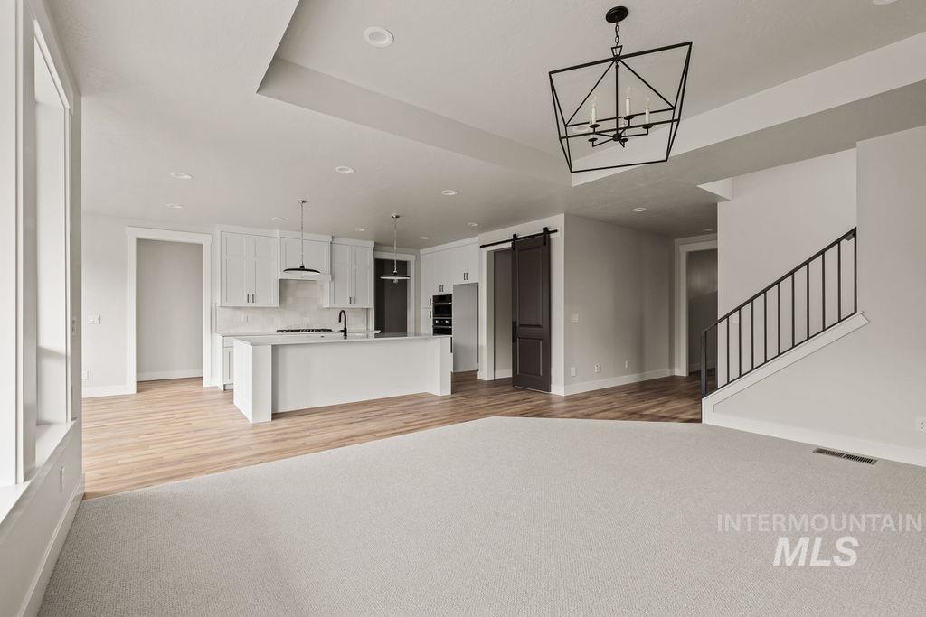 Unfurnished living room with a barn door, stairs, recessed lighting, a chandelier, and light colored carpet