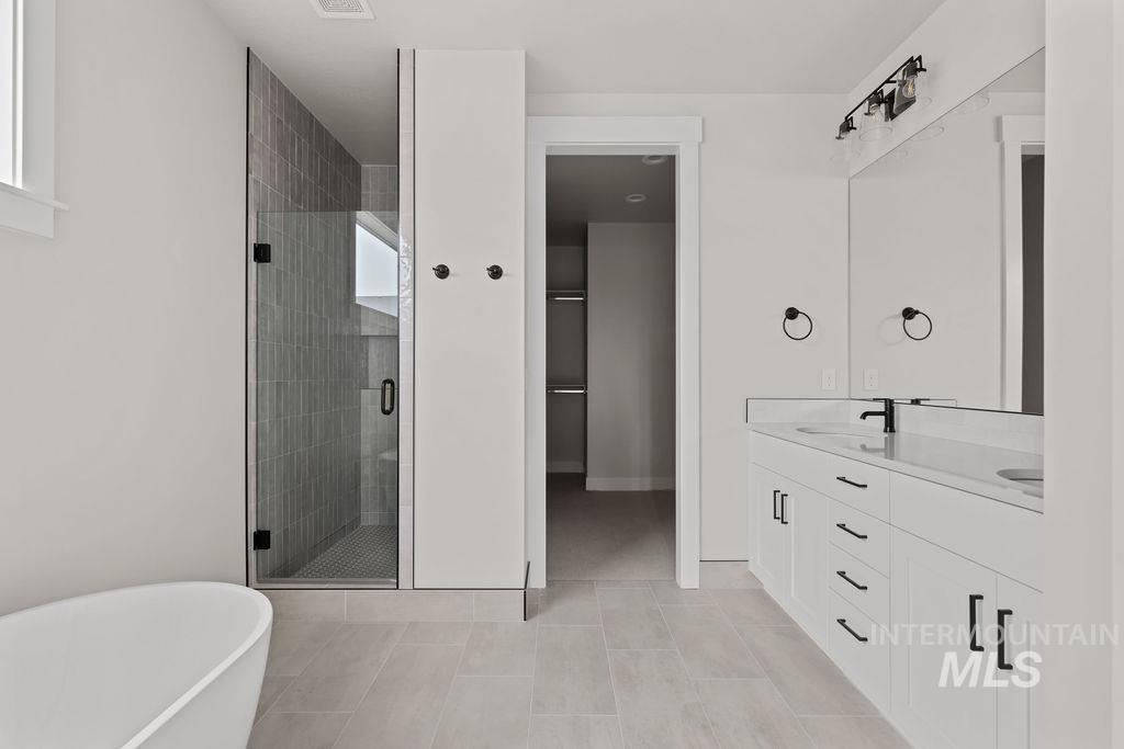 Full bath with double vanity, a freestanding tub, a shower stall, and light tile patterned floors