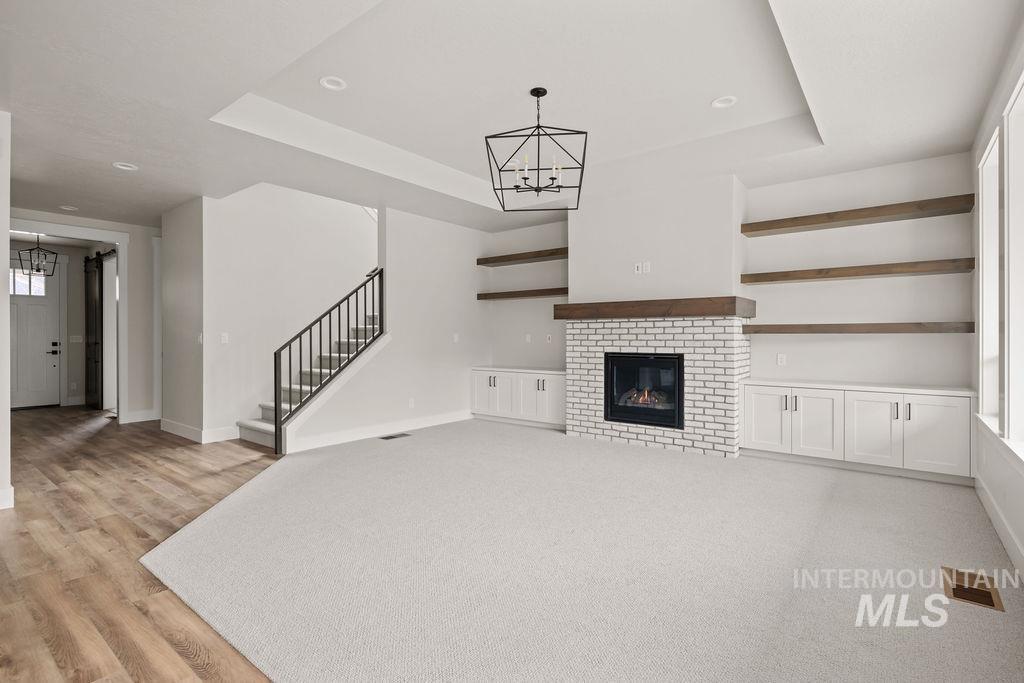 Unfurnished living room with a chandelier, a brick fireplace, a tray ceiling, stairway, and light wood finished floors