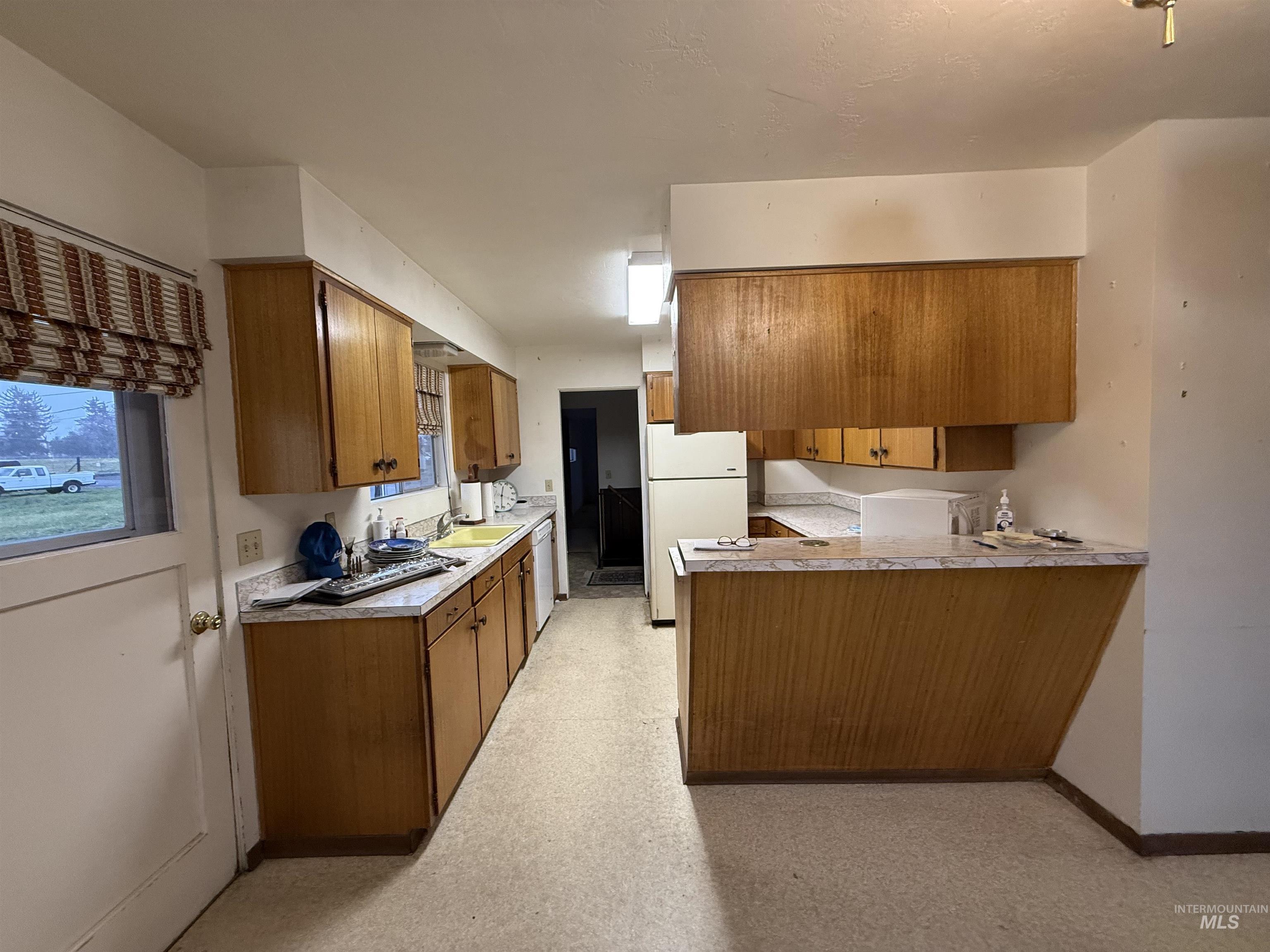 Kitchen featuring brown cabinetry, a peninsula, white appliances, and light countertops