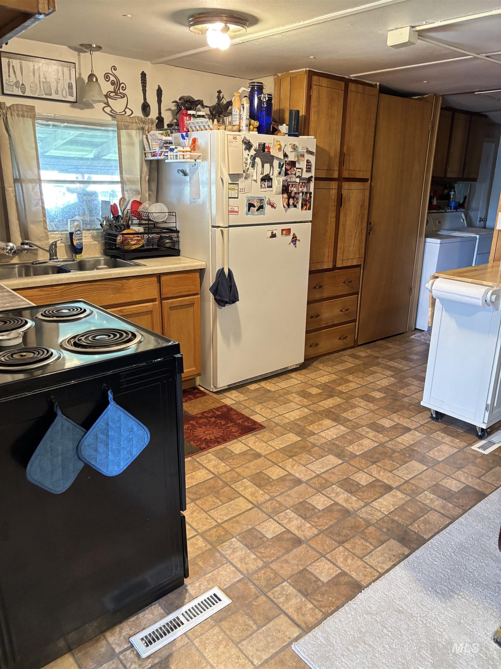 Kitchen with freestanding refrigerator, electric range oven, brown cabinetry, and brick patterned flooring