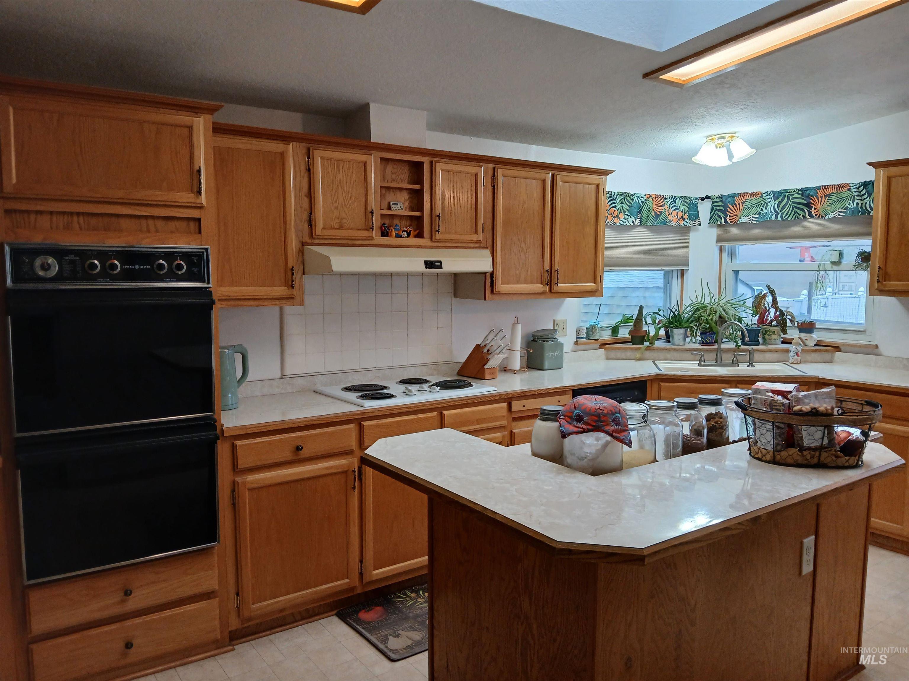Kitchen with light countertops, tasteful backsplash, brown cabinetry, a kitchen island, and under cabinet range hood