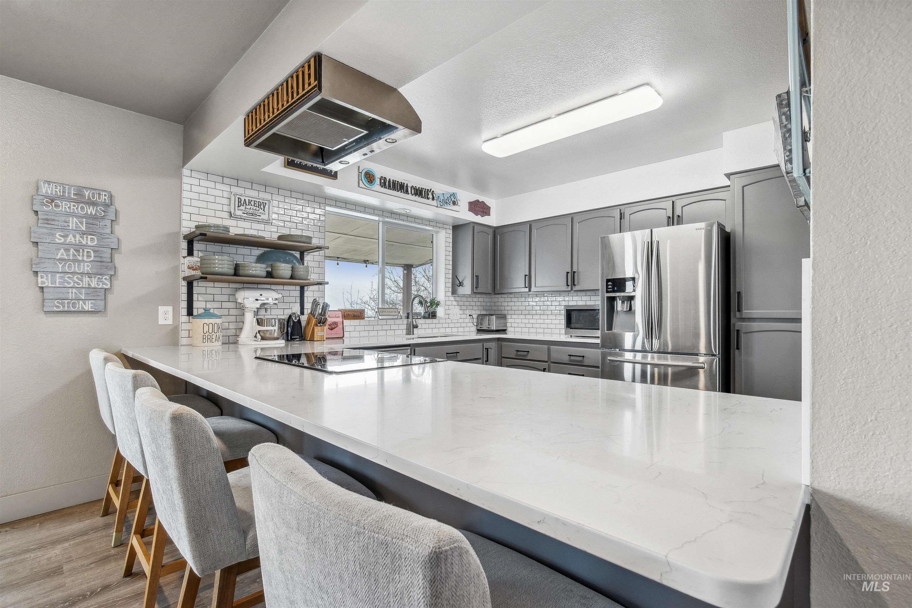Kitchen with gray cabinetry, a kitchen breakfast bar, appliances with stainless steel finishes, island exhaust hood, and a peninsula