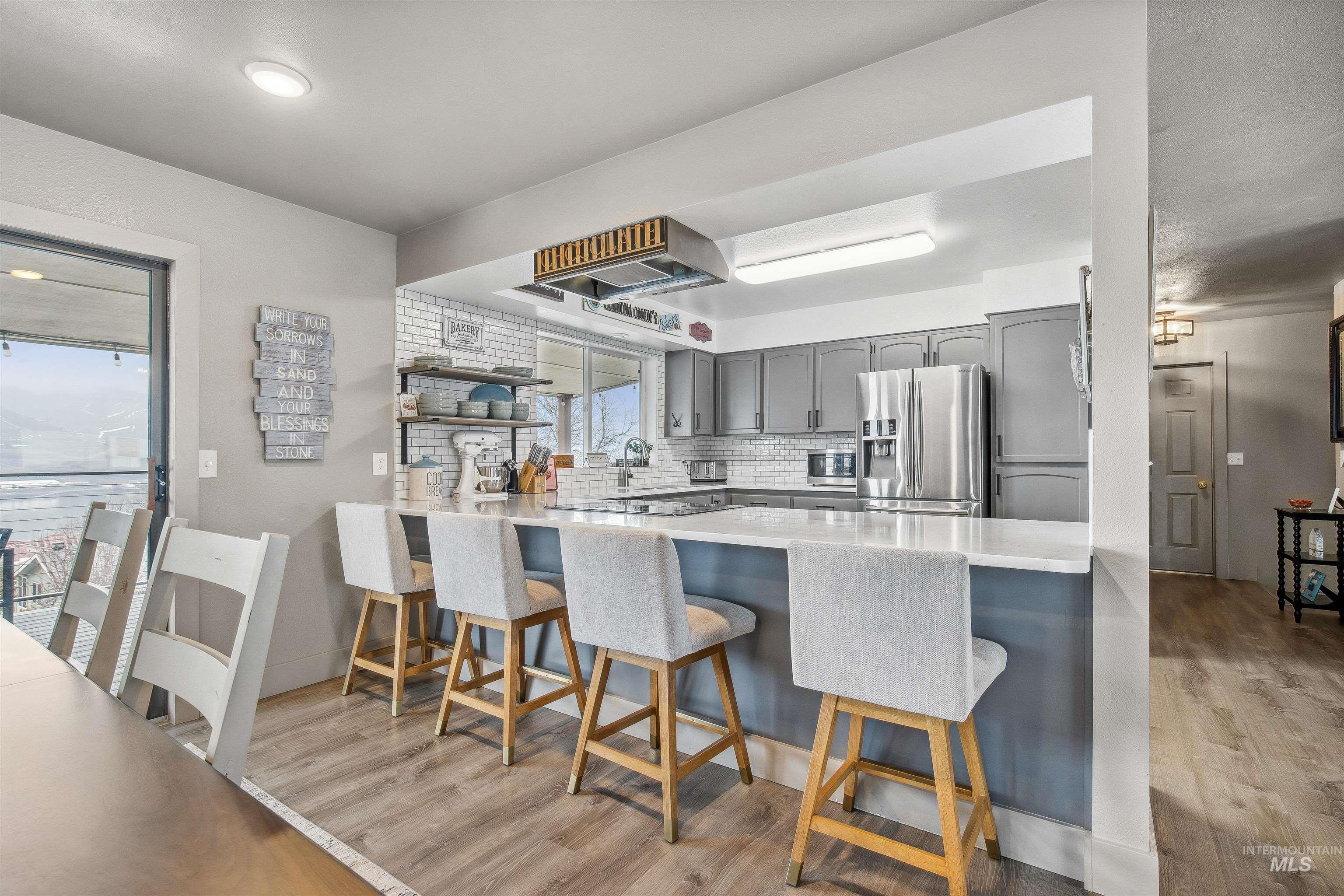 Kitchen with gray cabinetry, light wood finished floors, appliances with stainless steel finishes, a peninsula, and light stone counters