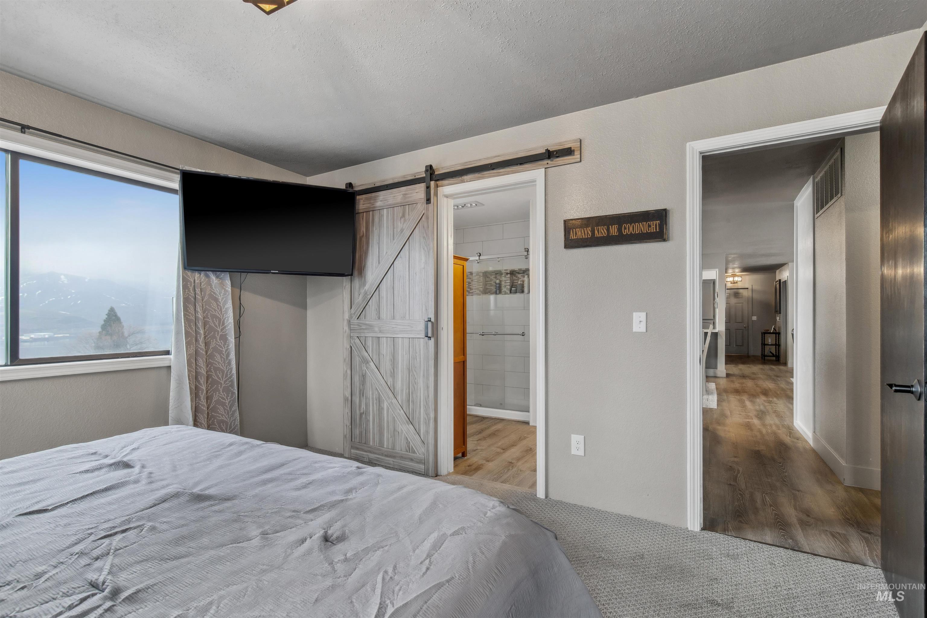 Bedroom featuring a barn door, wood finished floors, ensuite bathroom, and a textured ceiling