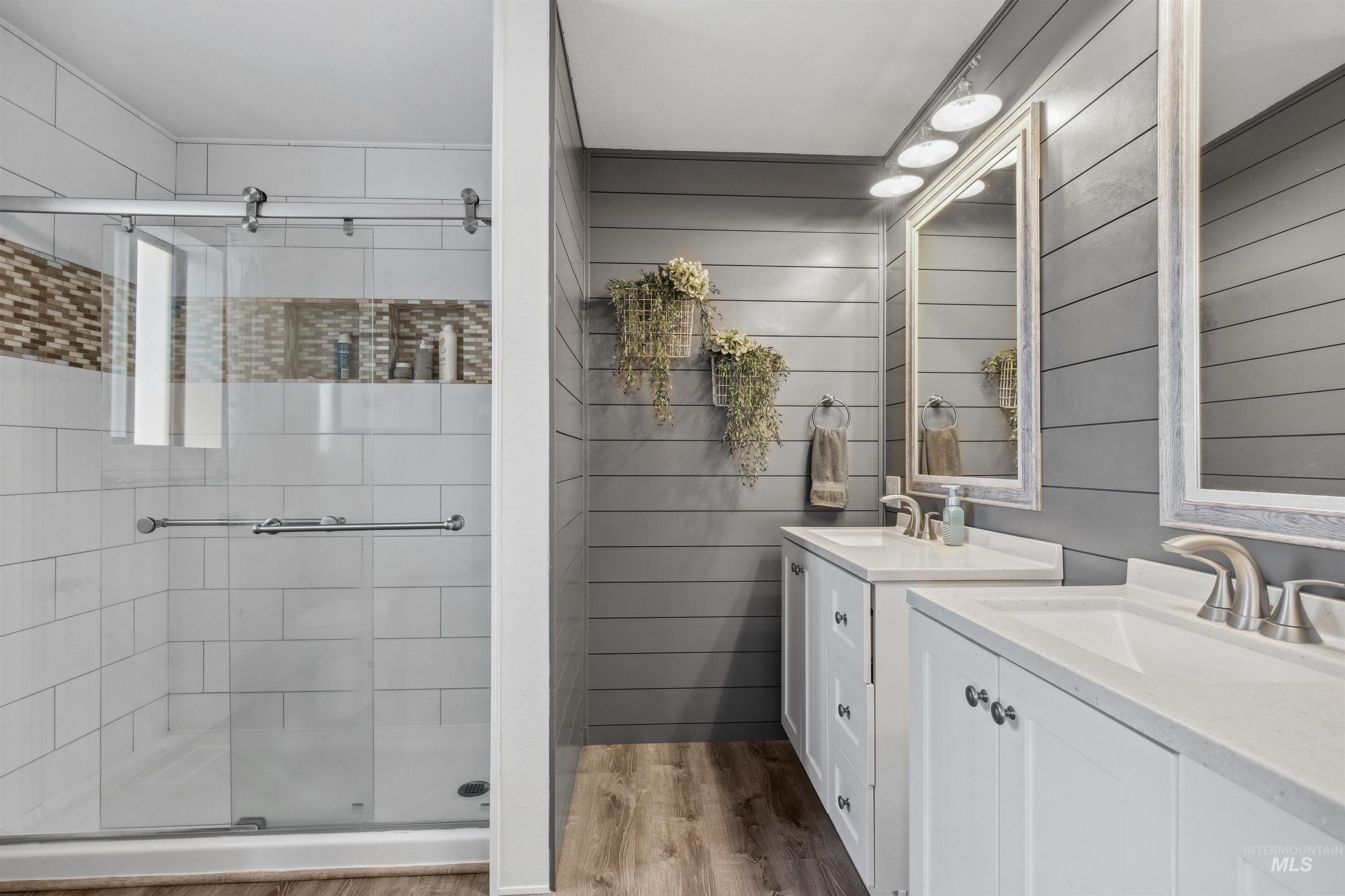 Bathroom featuring two vanities, a shower stall, wood walls, and light wood-style flooring