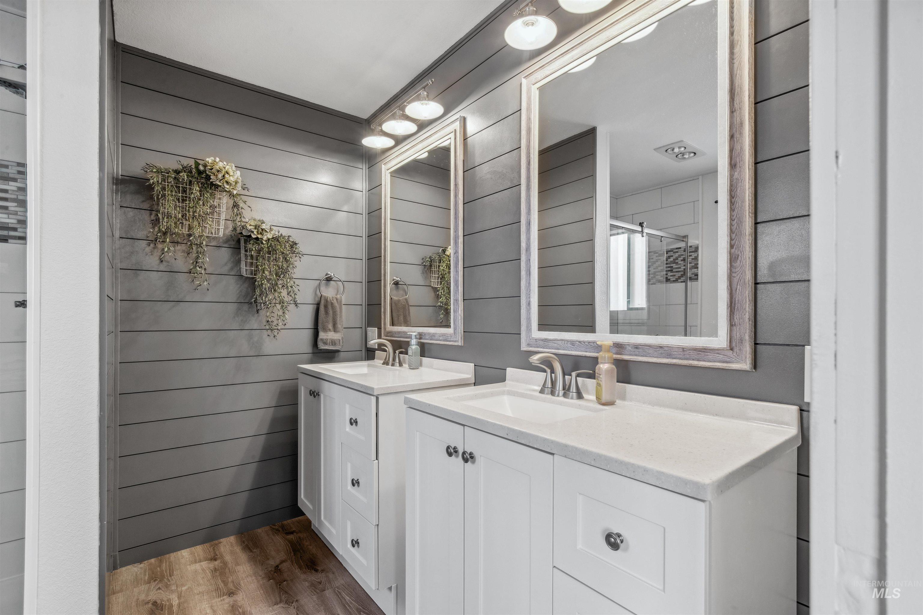 Bathroom featuring two vanities, light wood-type flooring, wooden walls, and a shower