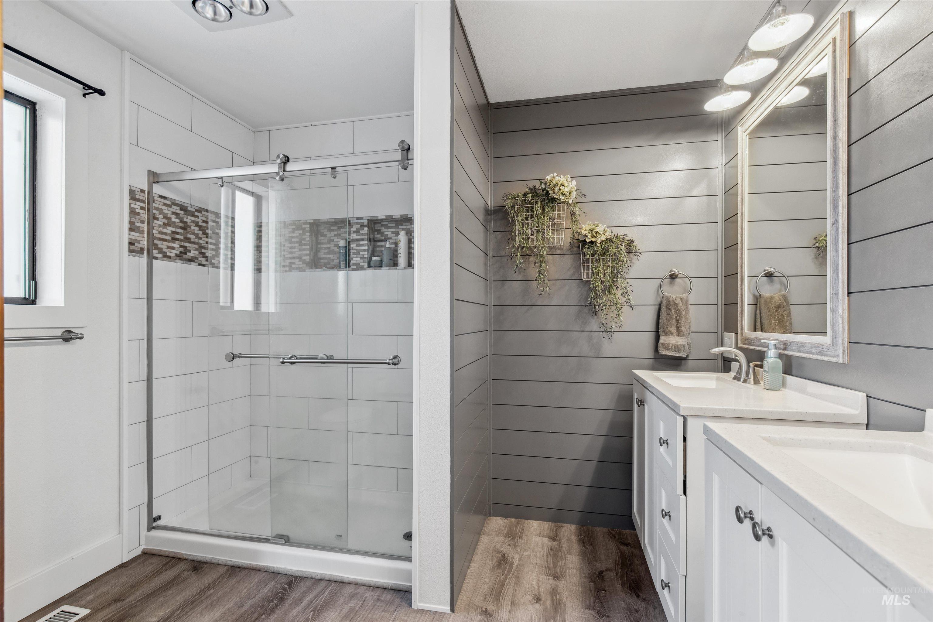Bathroom with two vanities, a stall shower, plenty of natural light, and light wood finished floors