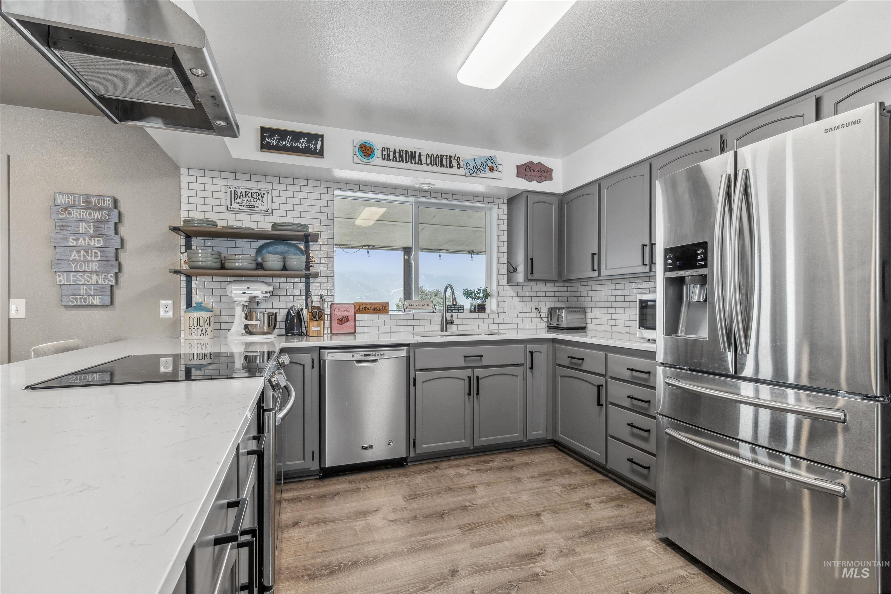 Kitchen featuring stainless steel appliances, gray cabinetry, range hood, light stone counters, and light wood-type flooring