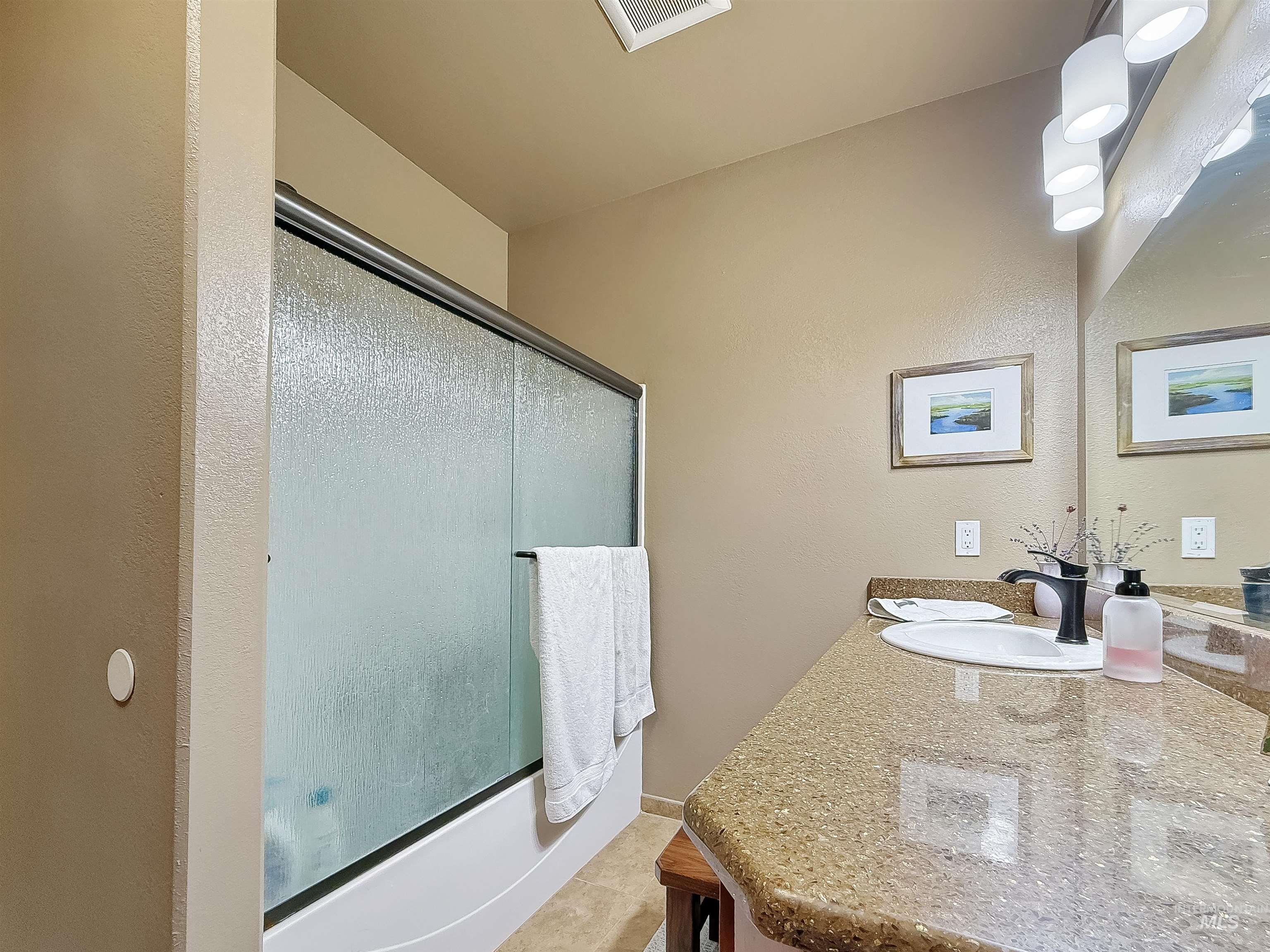 Bathroom featuring vanity, enclosed tub / shower combo, light tile patterned floors, and a textured wall