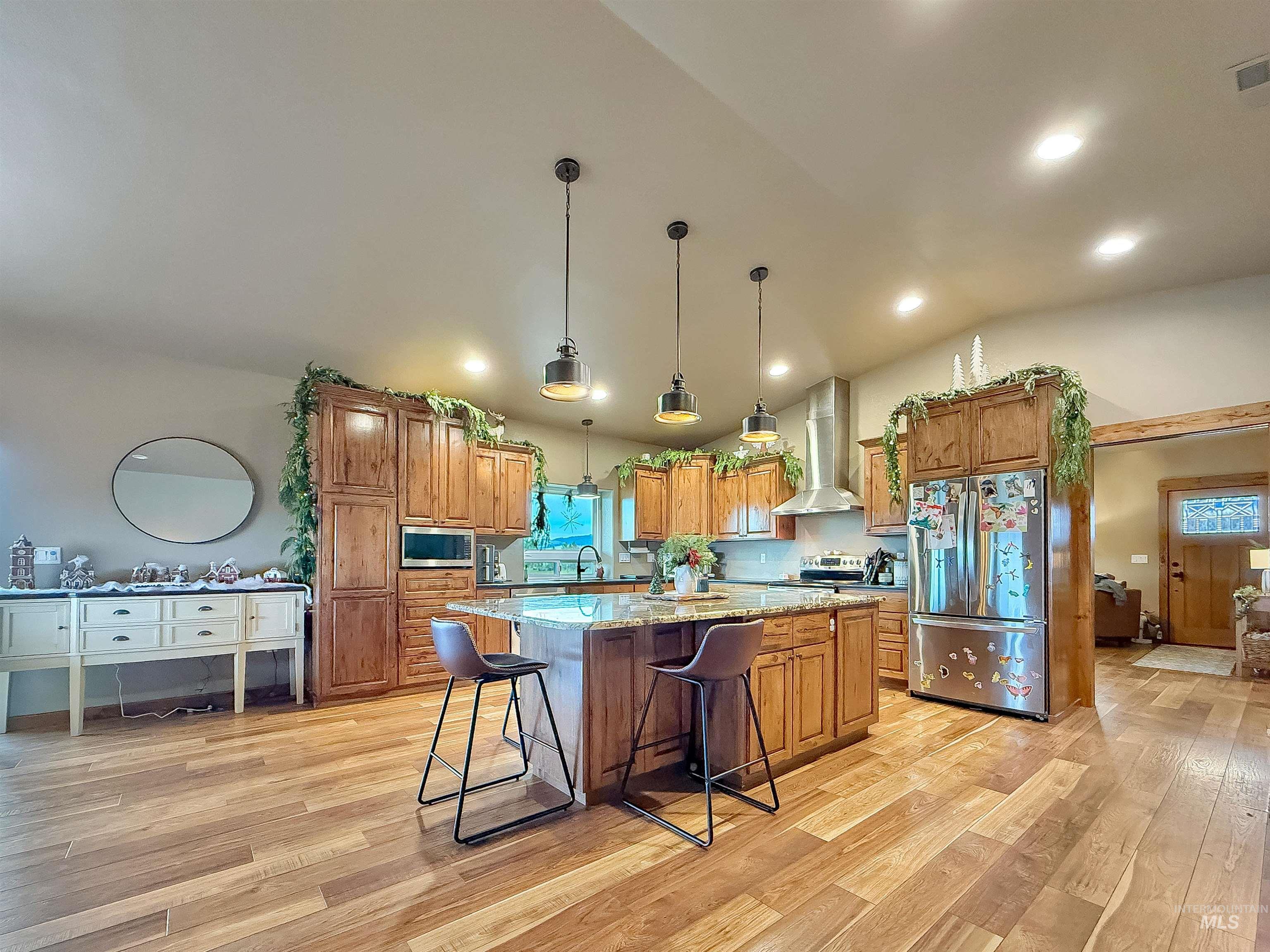 Kitchen with light stone counters, appliances with stainless steel finishes, brown cabinetry, a breakfast bar area, and vaulted ceiling