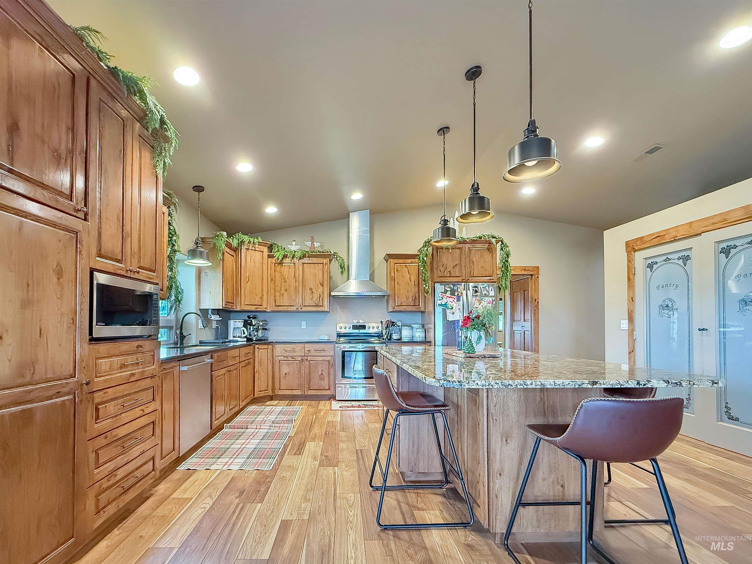 Kitchen featuring appliances with stainless steel finishes, lofted ceiling, a breakfast bar area, brown cabinetry, and light stone counters
