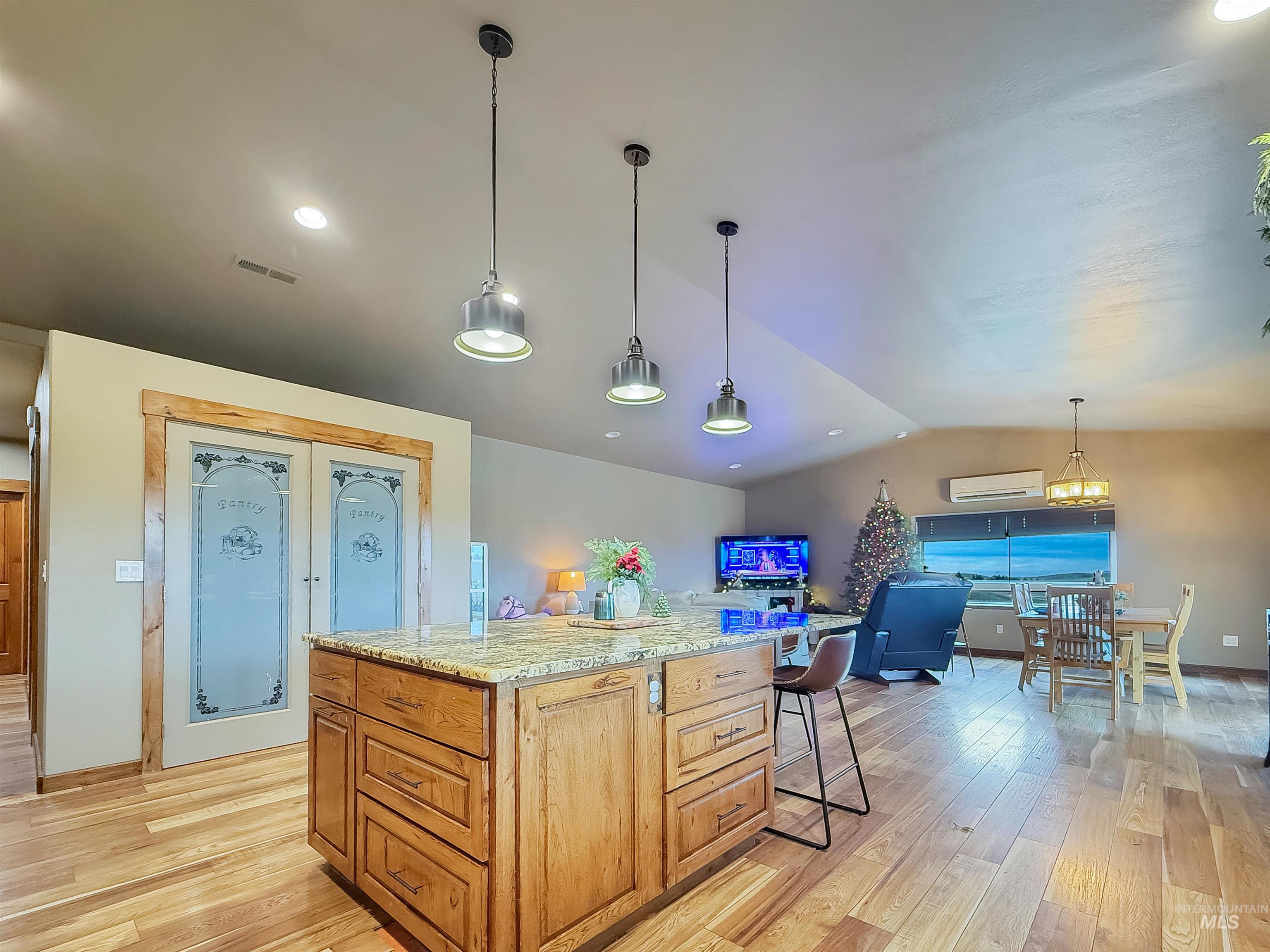 Kitchen with vaulted ceiling, decorative light fixtures, light stone countertops, brown cabinetry, and light wood-style flooring