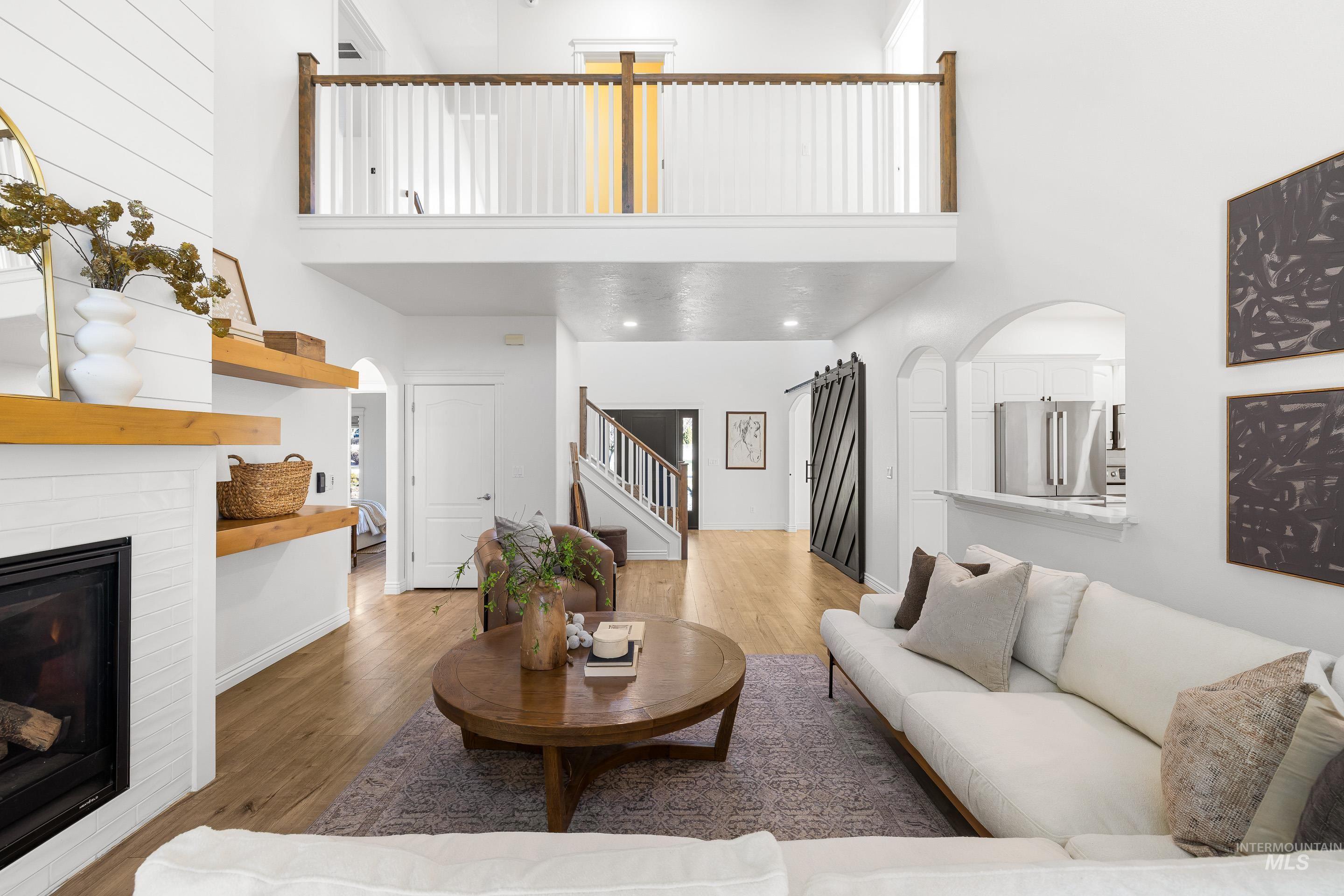 Living room with a towering ceiling, a glass covered fireplace, wood finished floors, stairway, and arched walkways