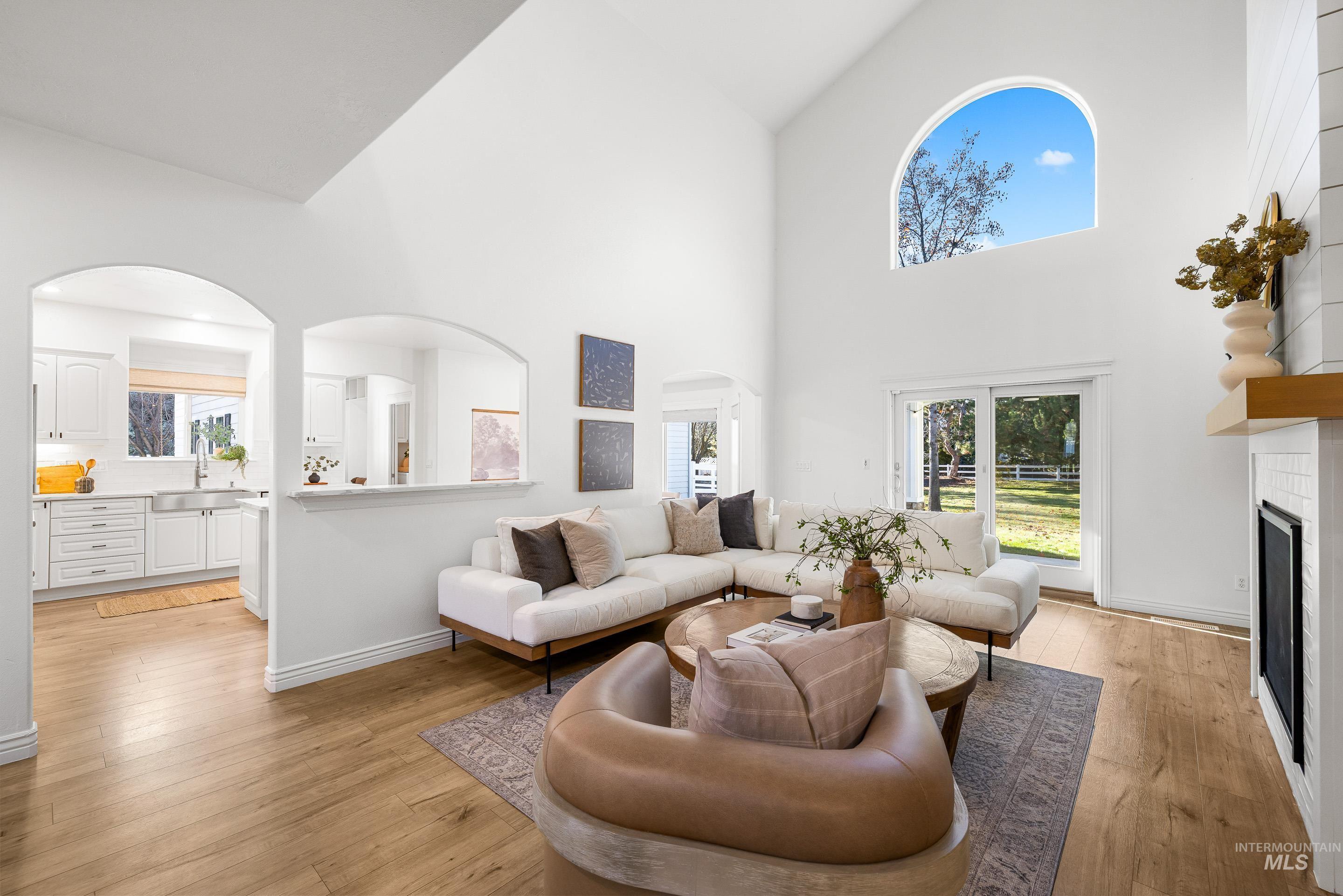 Living room with arched walkways, high vaulted ceiling, light wood-style flooring, and a glass covered fireplace