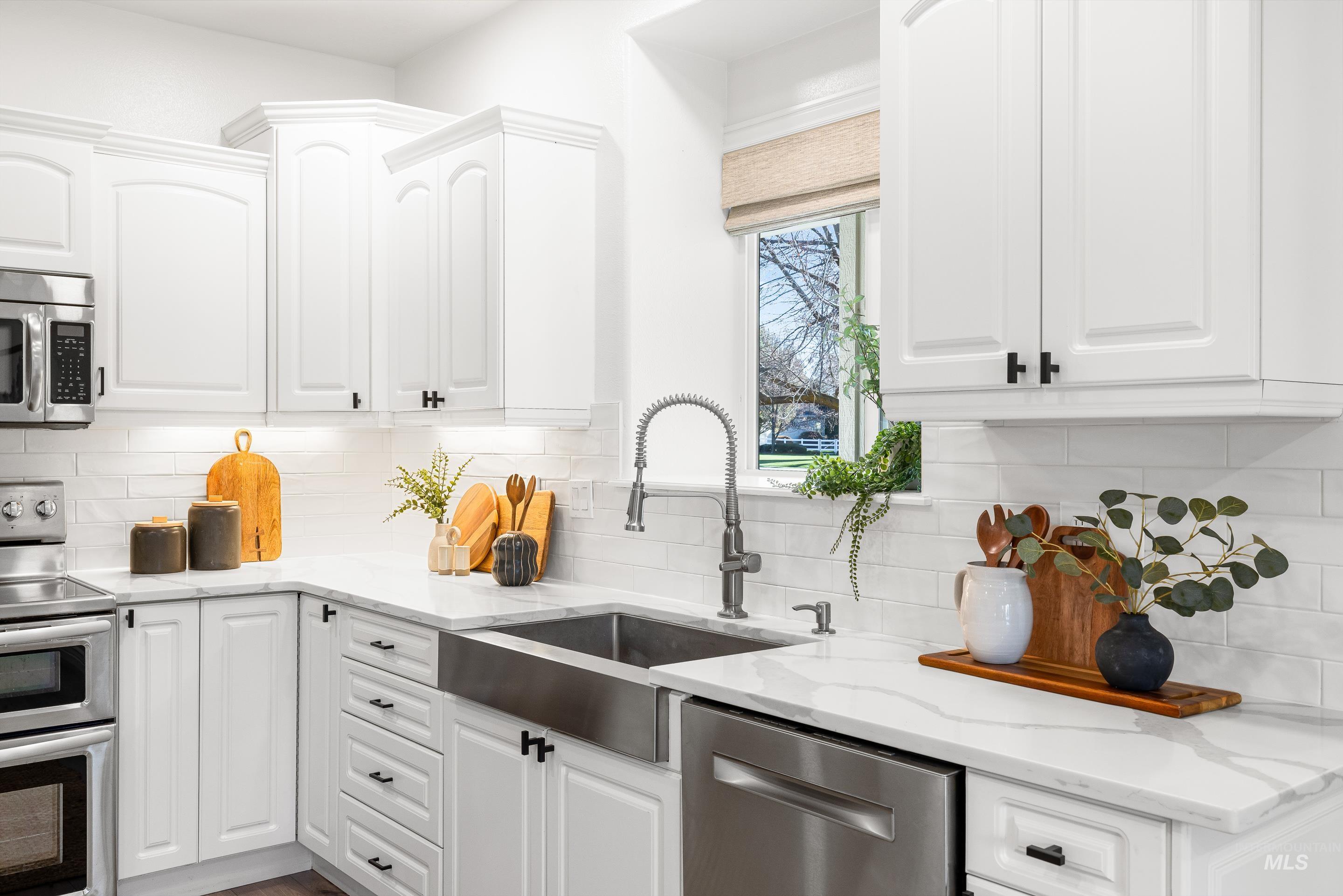 Kitchen with appliances with stainless steel finishes, white cabinets, light stone counters, and backsplash