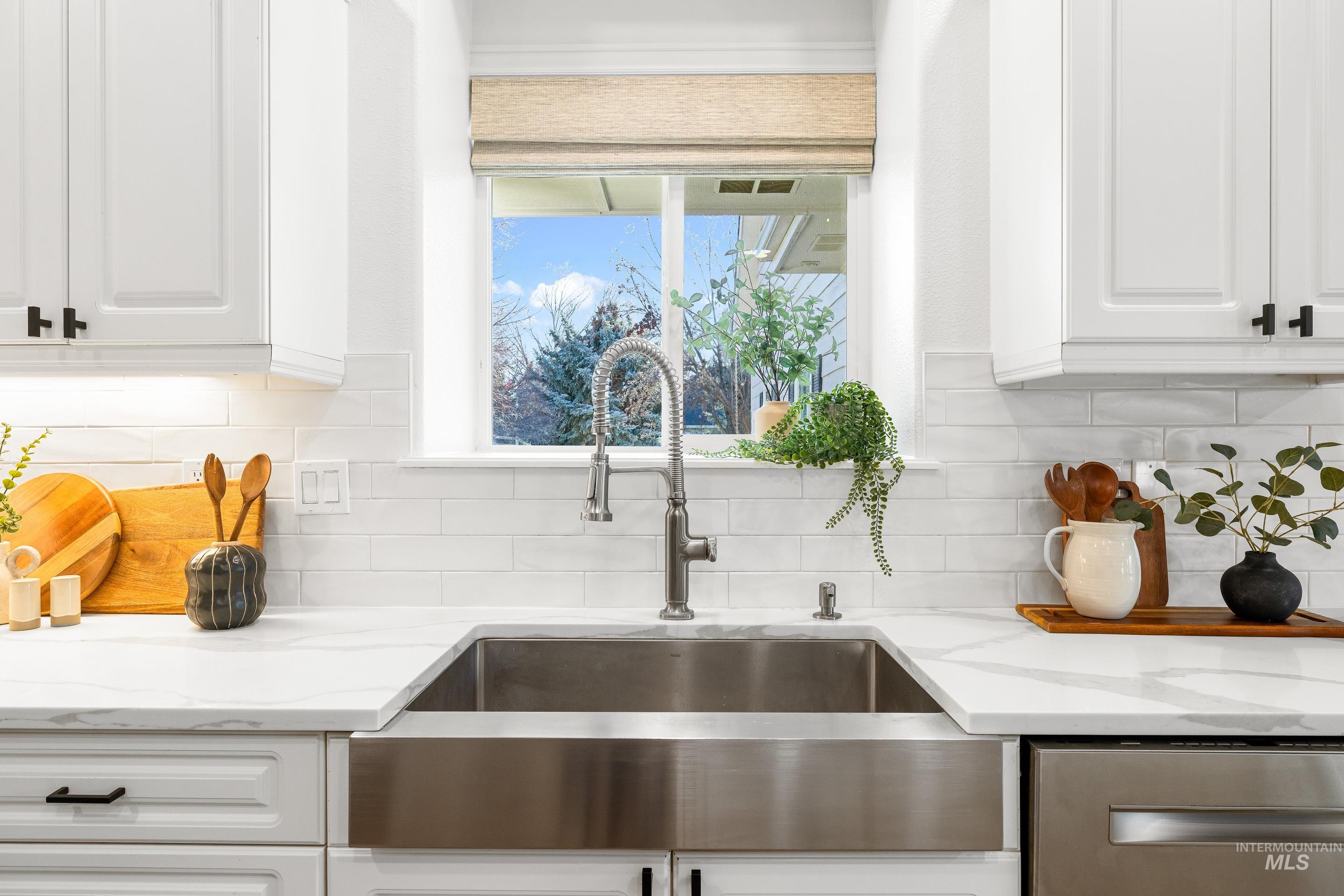 Kitchen view of light stone counters, white cabinets, dishwasher, and tasteful backsplash