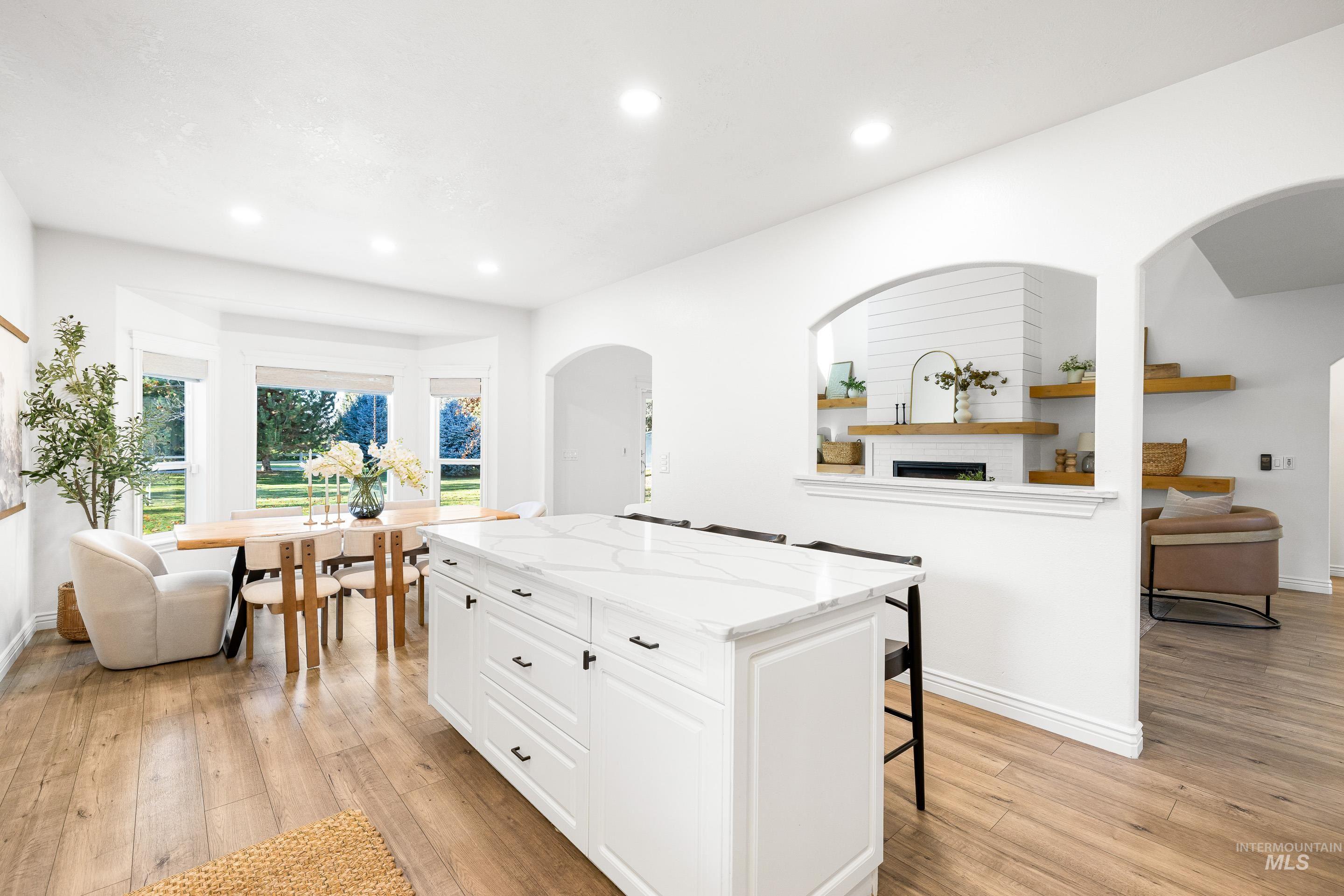 Kitchen featuring arched walkways, light stone countertops, white cabinets, a kitchen bar, and a kitchen island